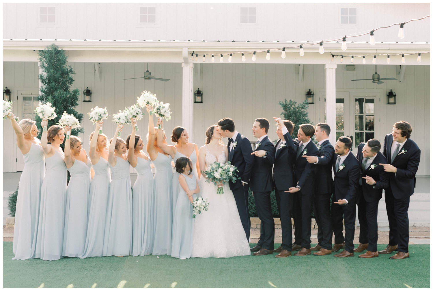 bride and groom kissing outdoors with bridal party celebrating around them
