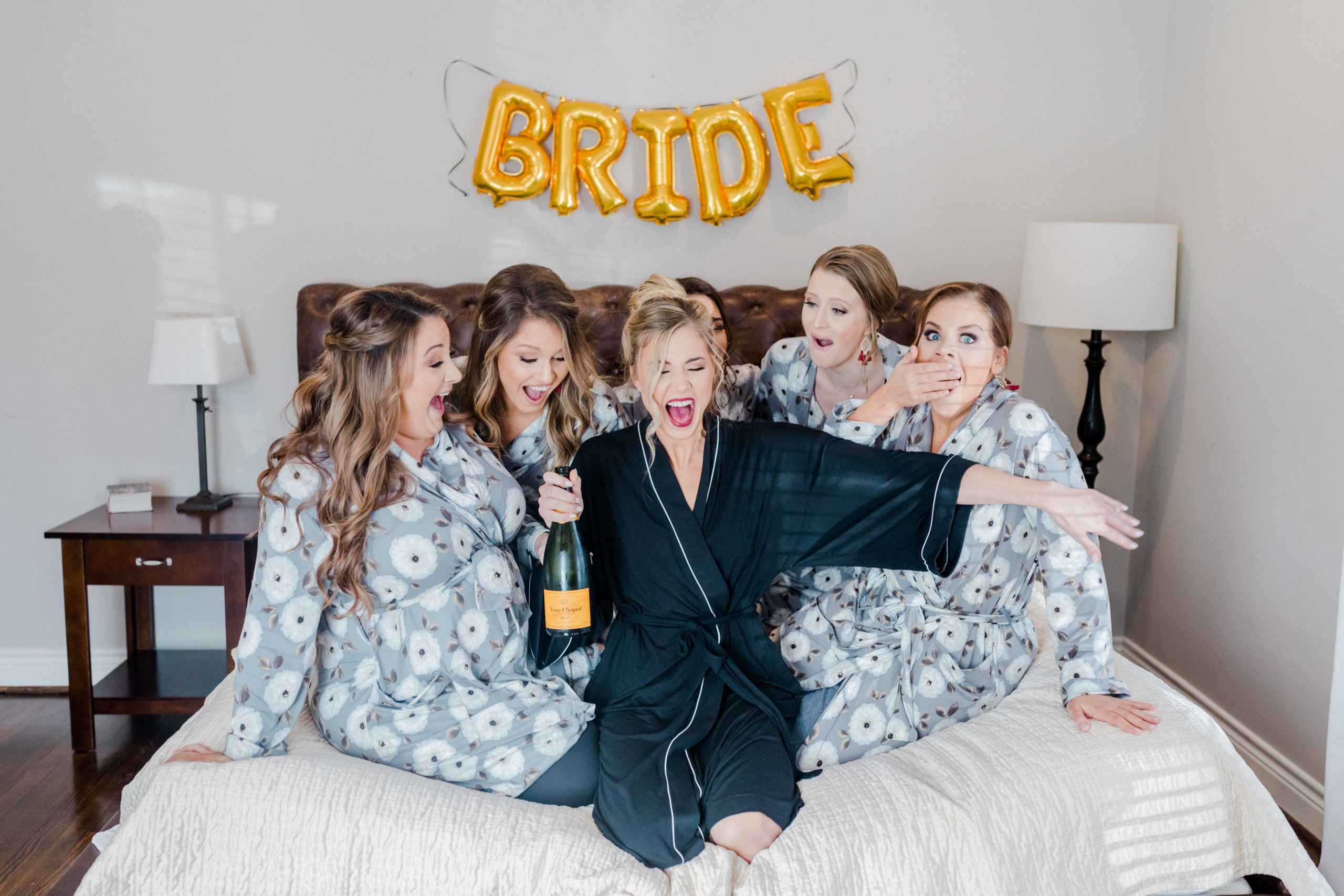 Bride & Bridesmaids popping champagne on a bed