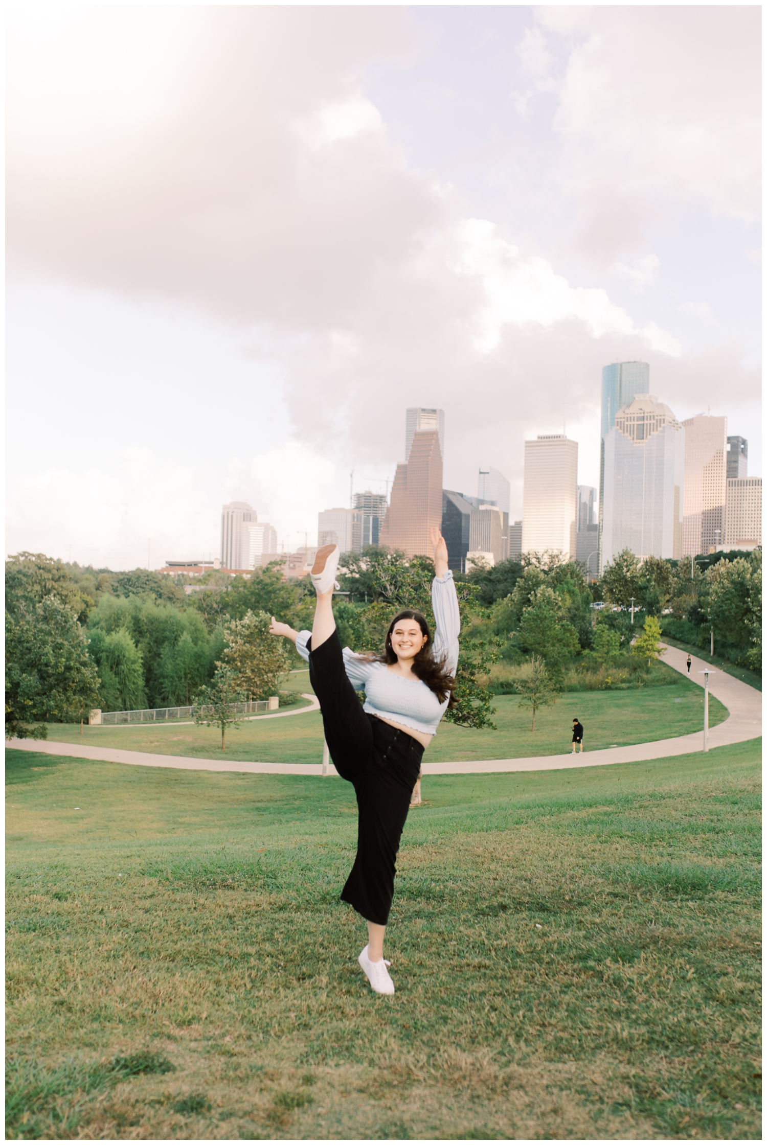 girl kicking leg in front of Houston skyline for her senior session with Reed Gallagher Photography at Buffalo Bayou Park in Houston Texas
