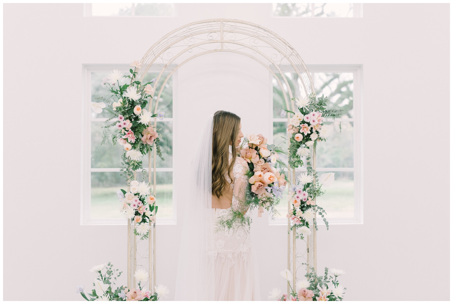 a bride posing with her bouquet under a floral arch in a natural light wedding chapel