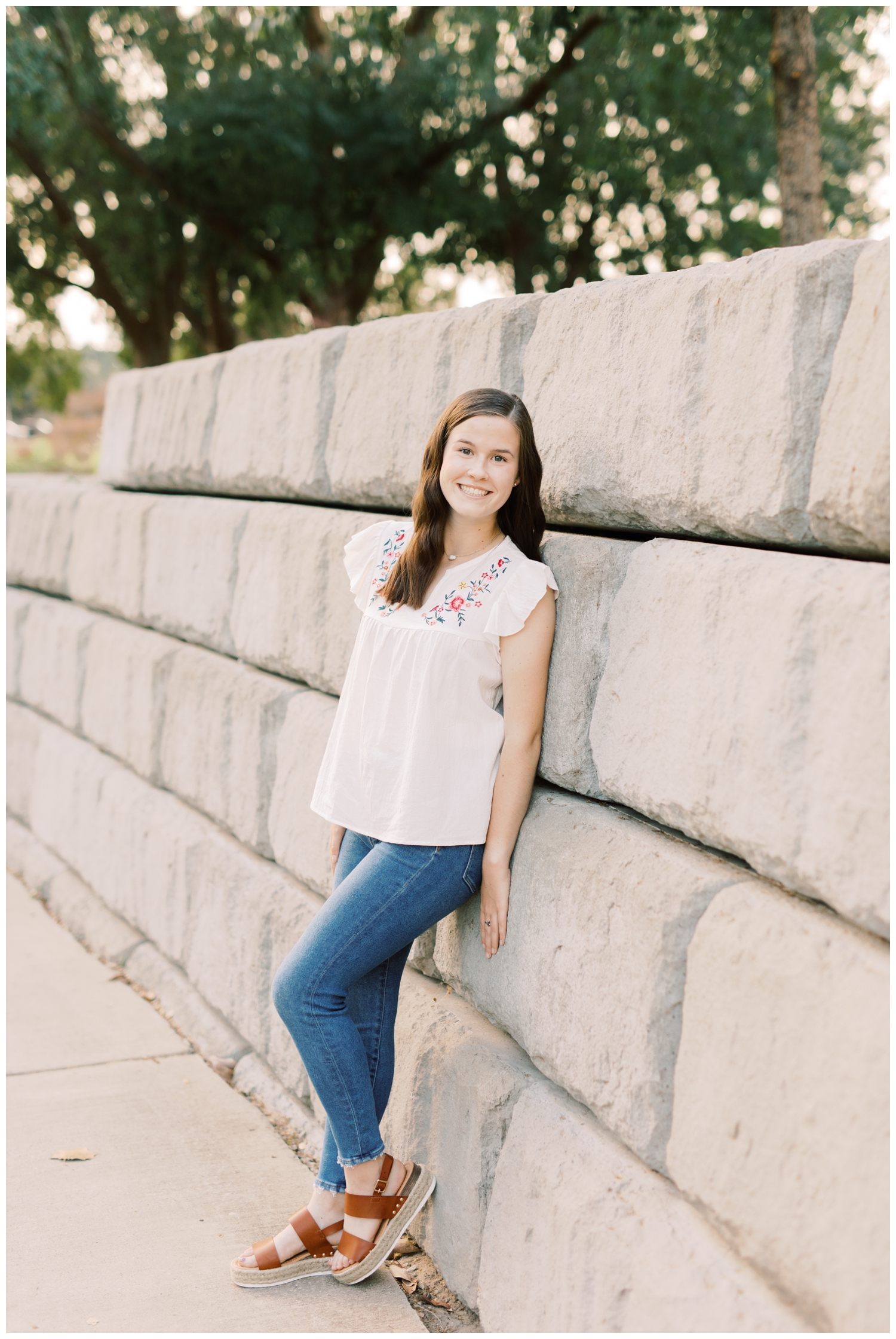 a high school senior leaning against a gray column wall for her houston photography senior session