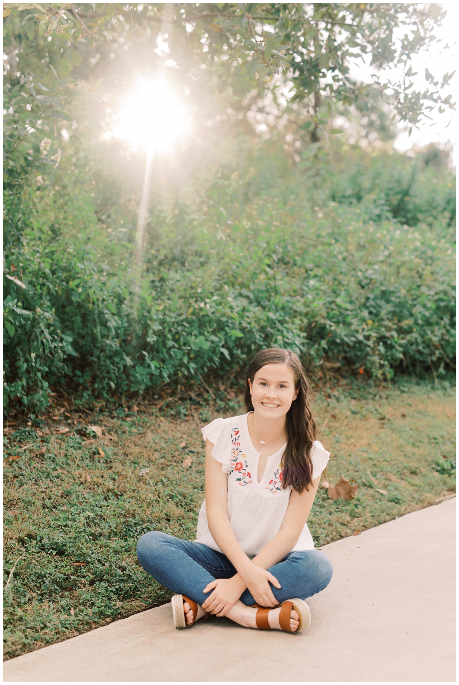 high school senior girl sitting on the ground near a field in Houston