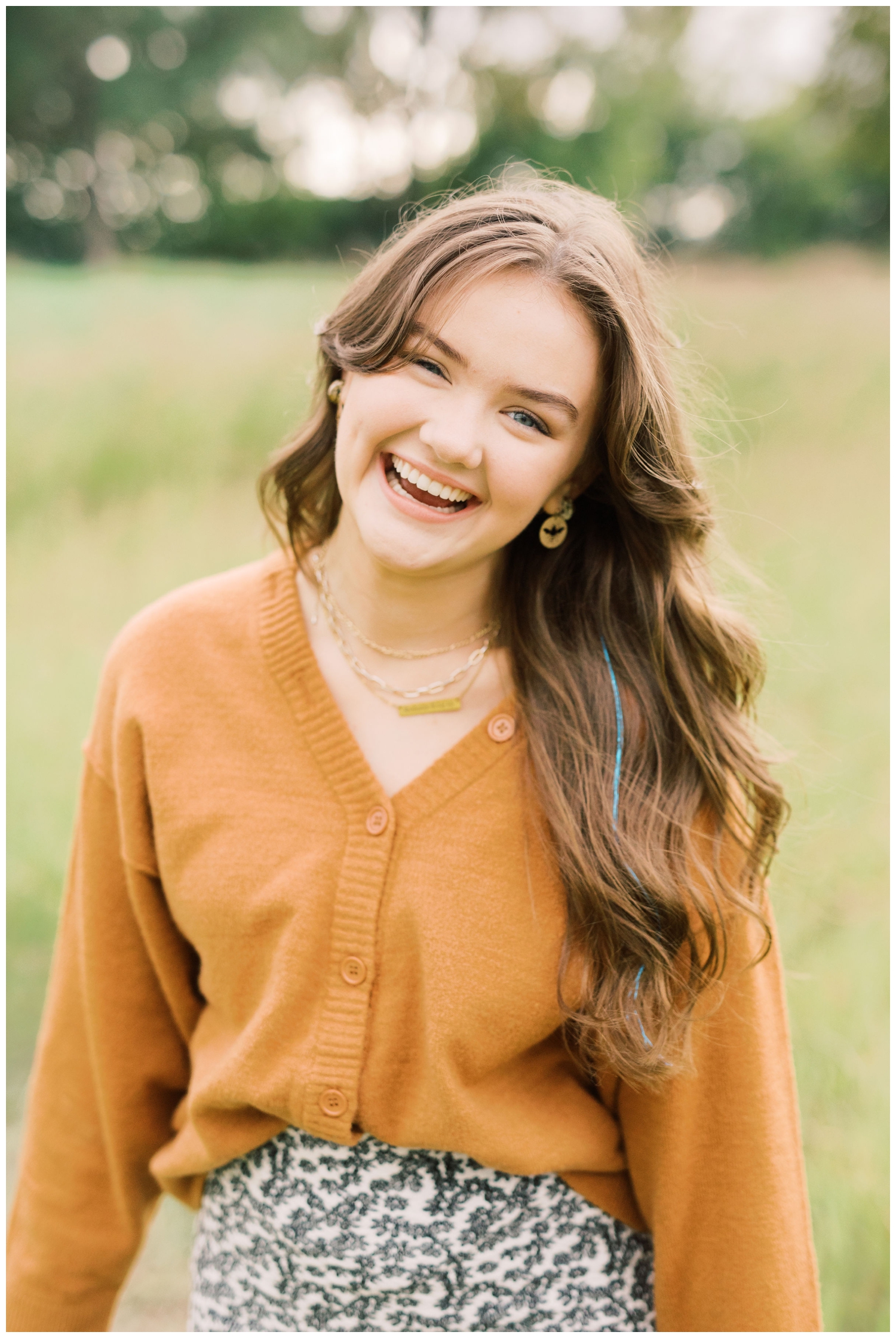 high school senior smiling in rust colored sweater in a field in Houston Texas