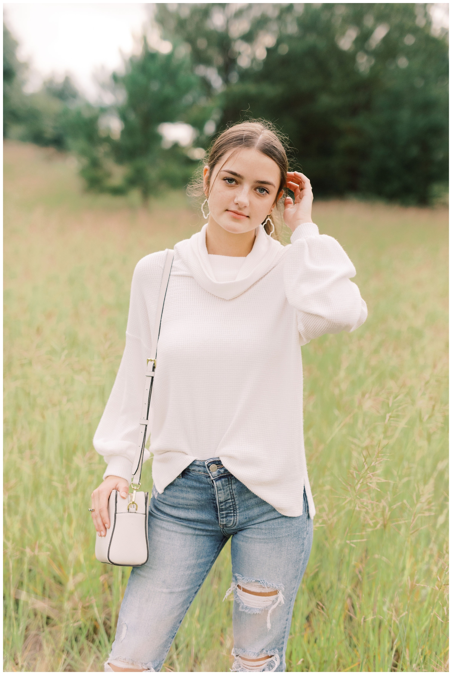 high school portrait of girl standing in cream sweater in a field