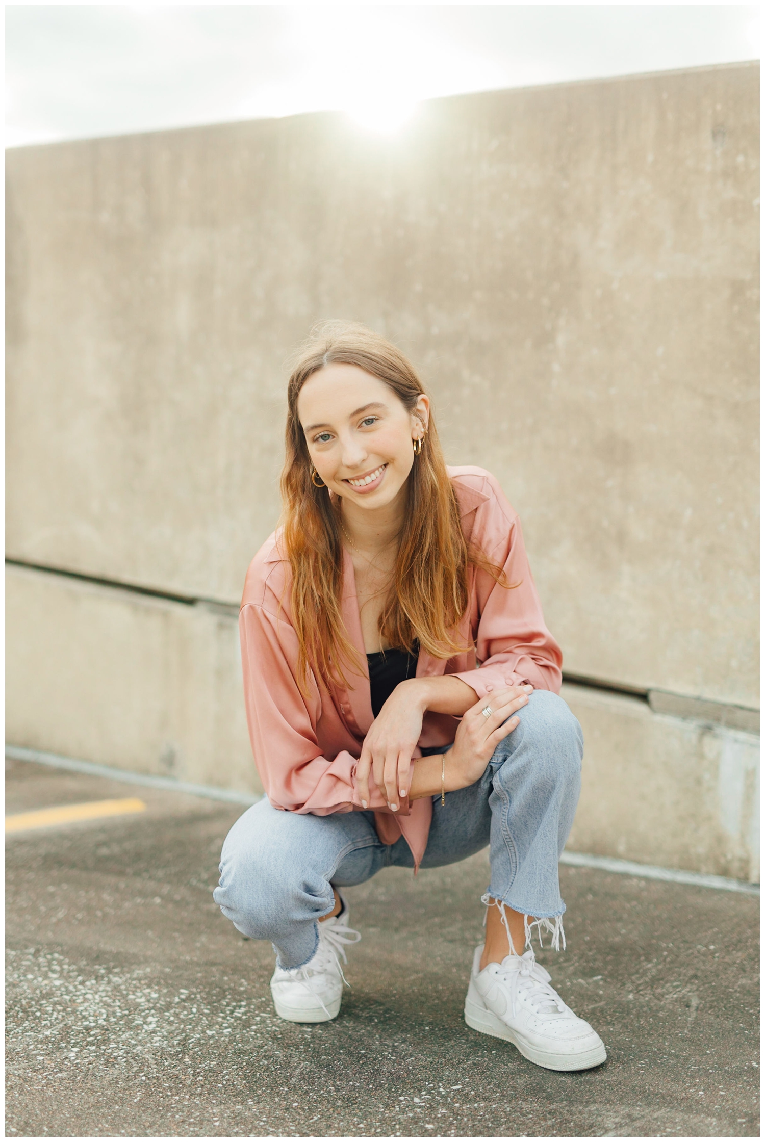 girl squatting on ground in denim jeans and blush shirt