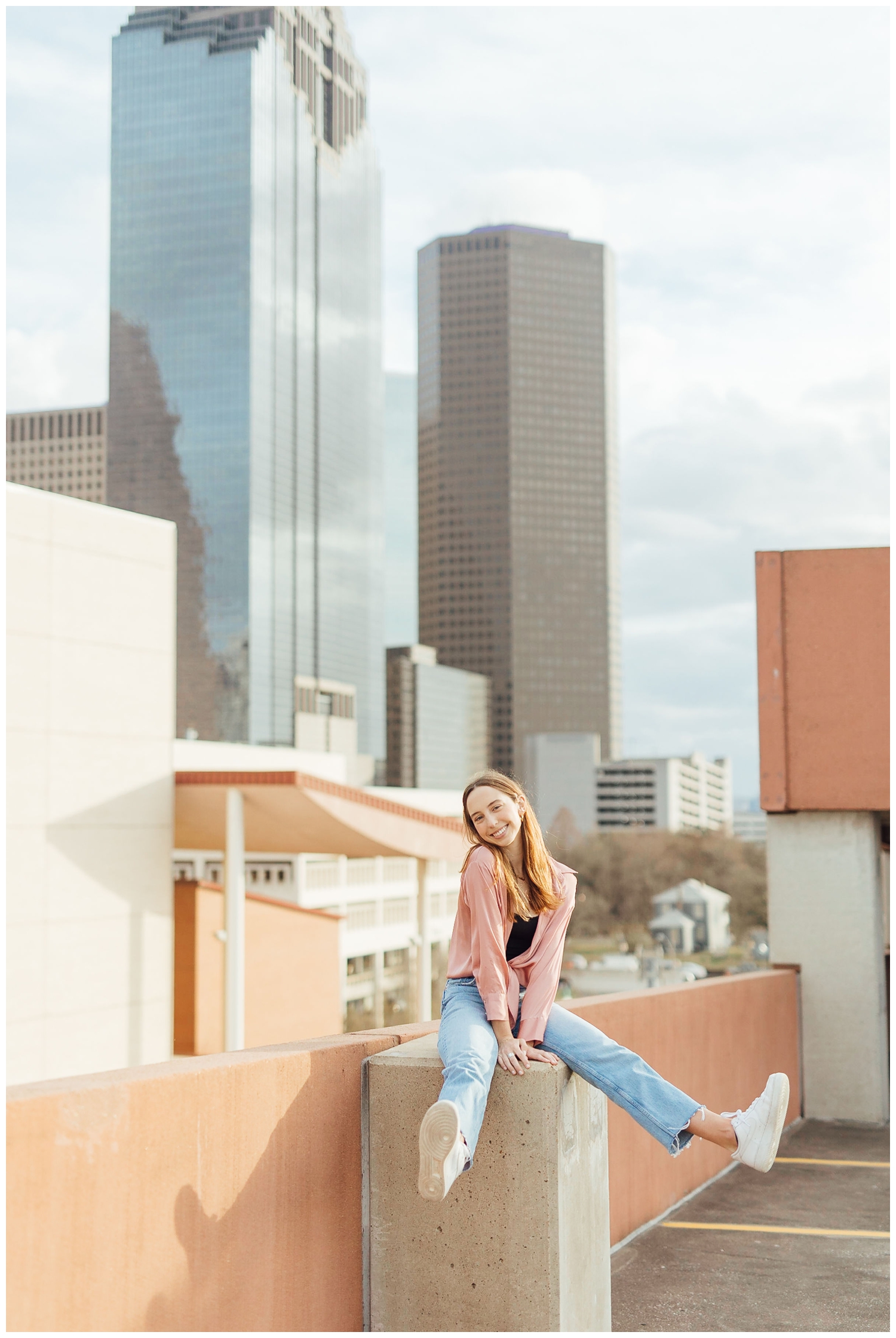 girl sitting on rail in front of Houston skyline for Downtown Houston senior photos
