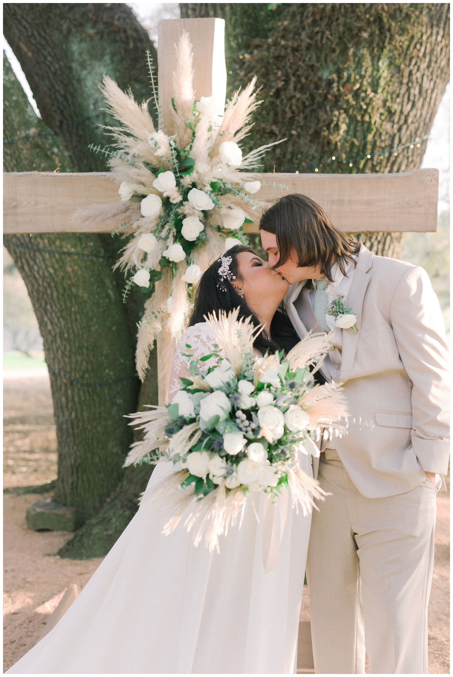 bride and groom kissing by floral cross