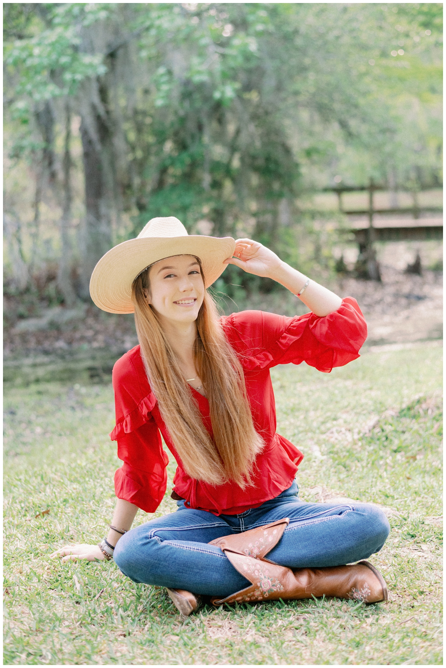 girl sitting in a field tipping her cowboy hat