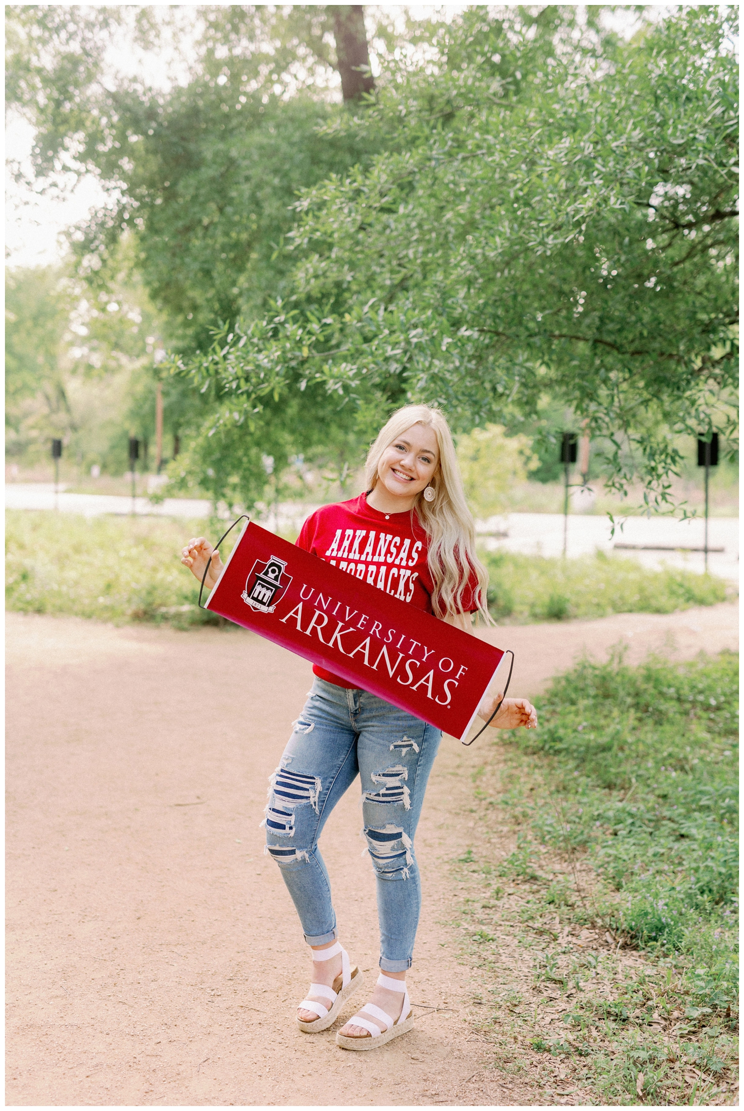 girl standing on sidewalk holding Arkansas college sign at Houston Arboretum Senior Portraits