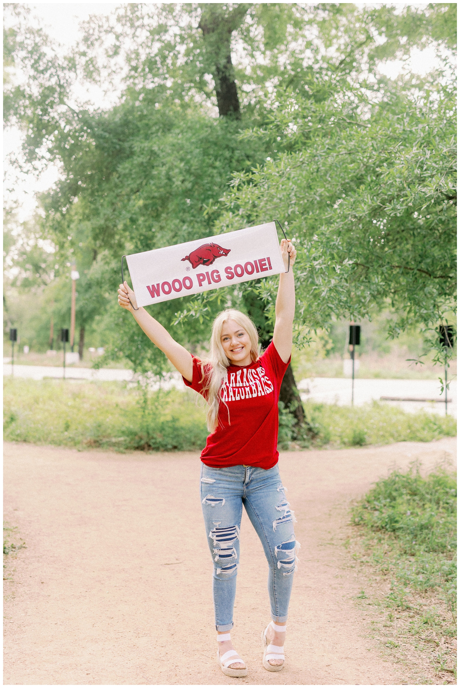 girl holding University of Arkansas sign over her head for Houston Arboretum Senior Portraits