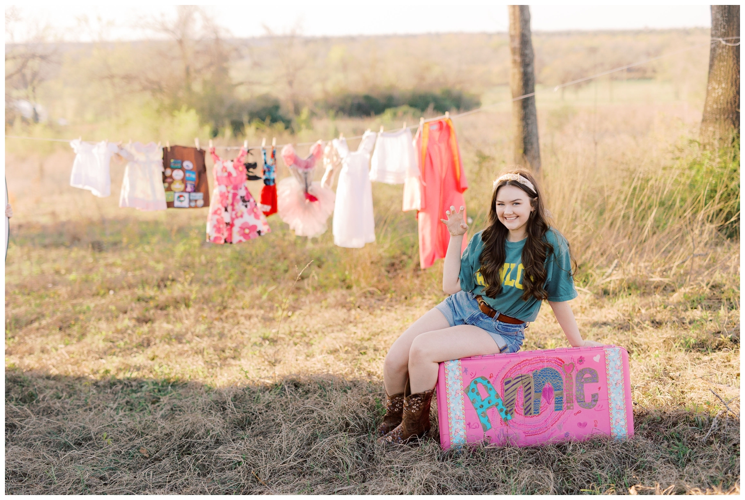 senior girl sitting on camp trunk under clothesline in a field