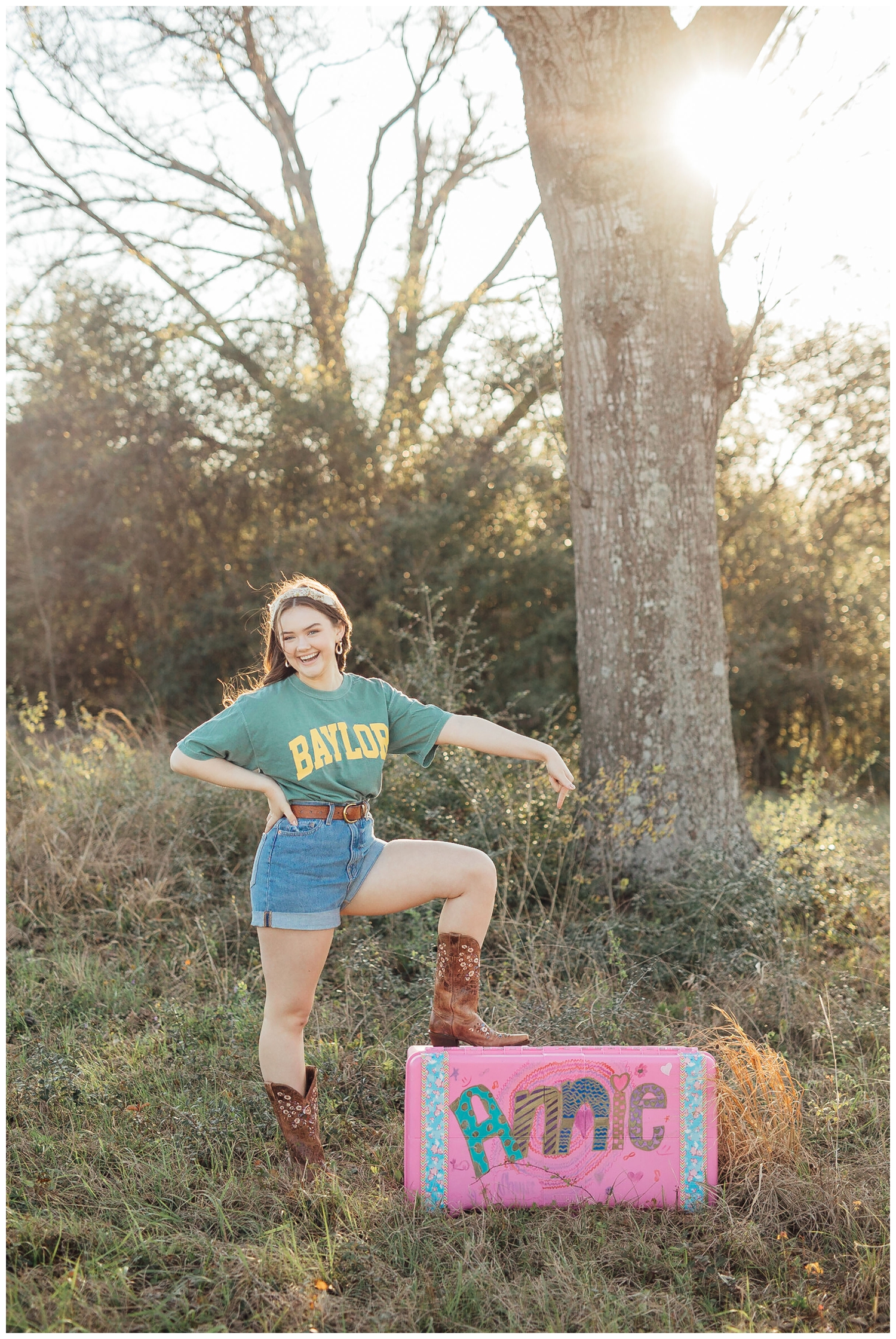girl standing by a tree with cowboy boots and college shirt posing for a Houston Outdoor senior photographer