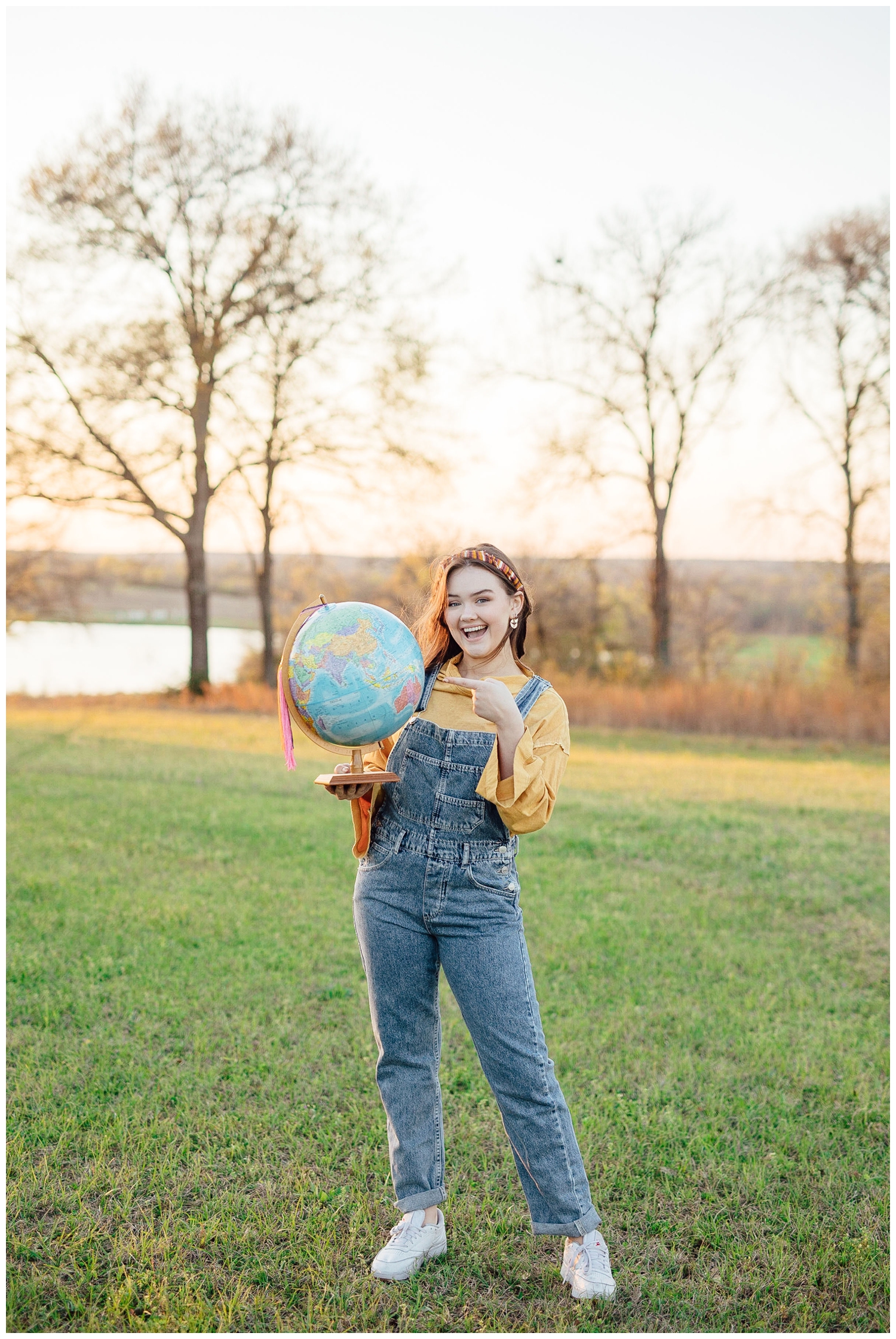 senior girl in overalls holding a globe in a field
