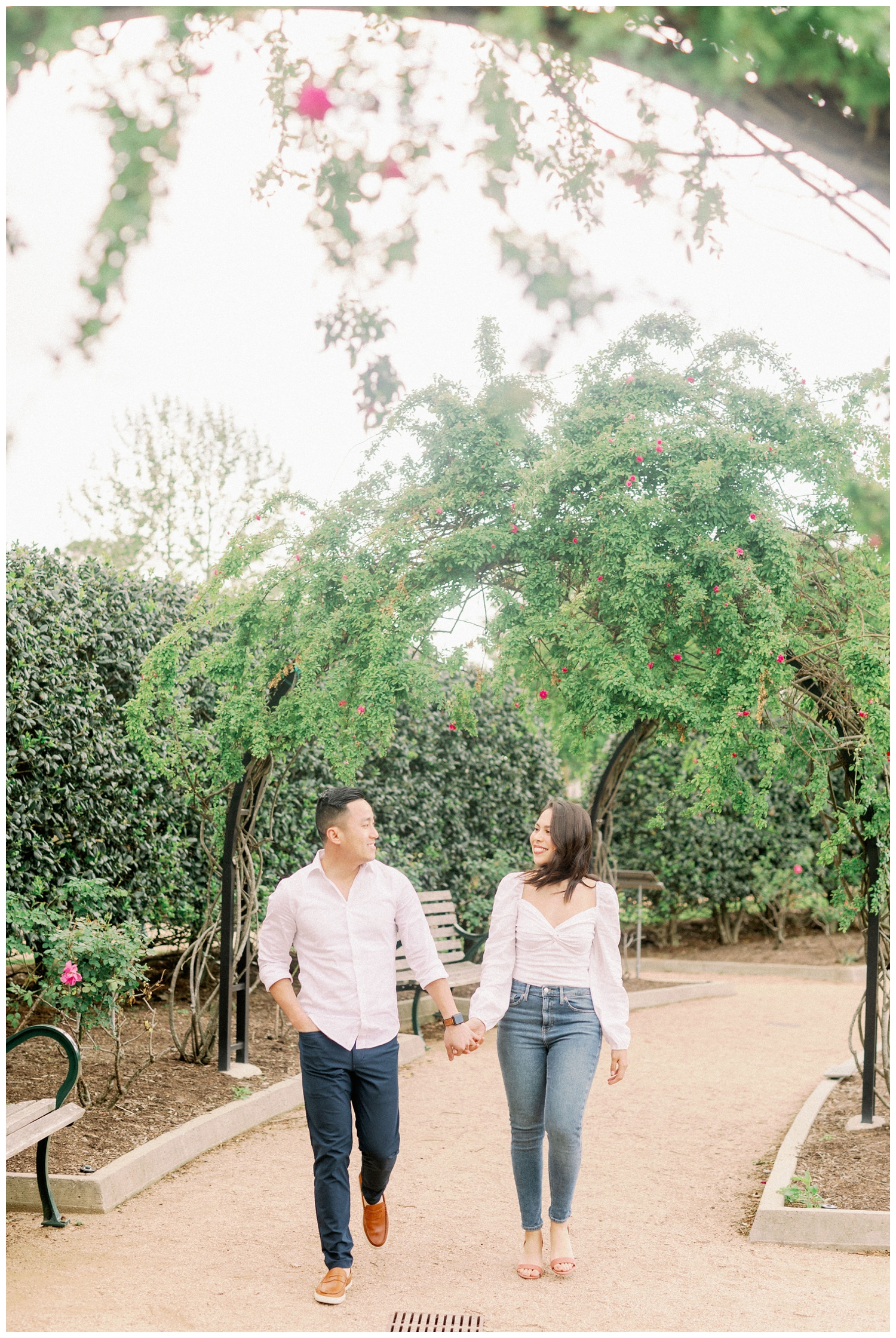 couple holding hands walking under green archway