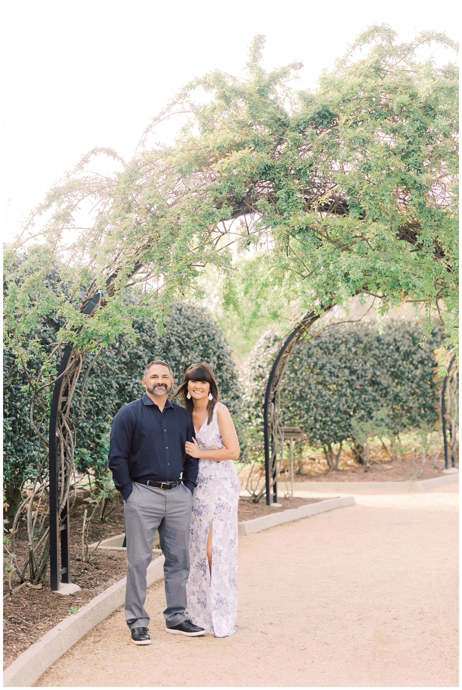 couple posing and smiling underneath greenery arch outdoors in Houston Texas