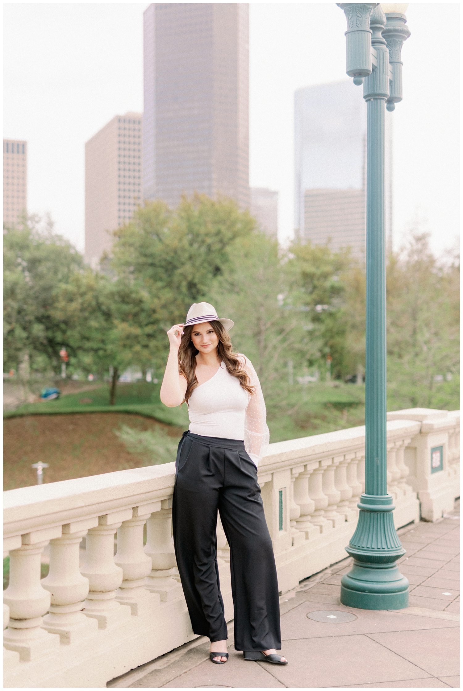 senior girl posing on bridge in front of Houston Skyline in a hat