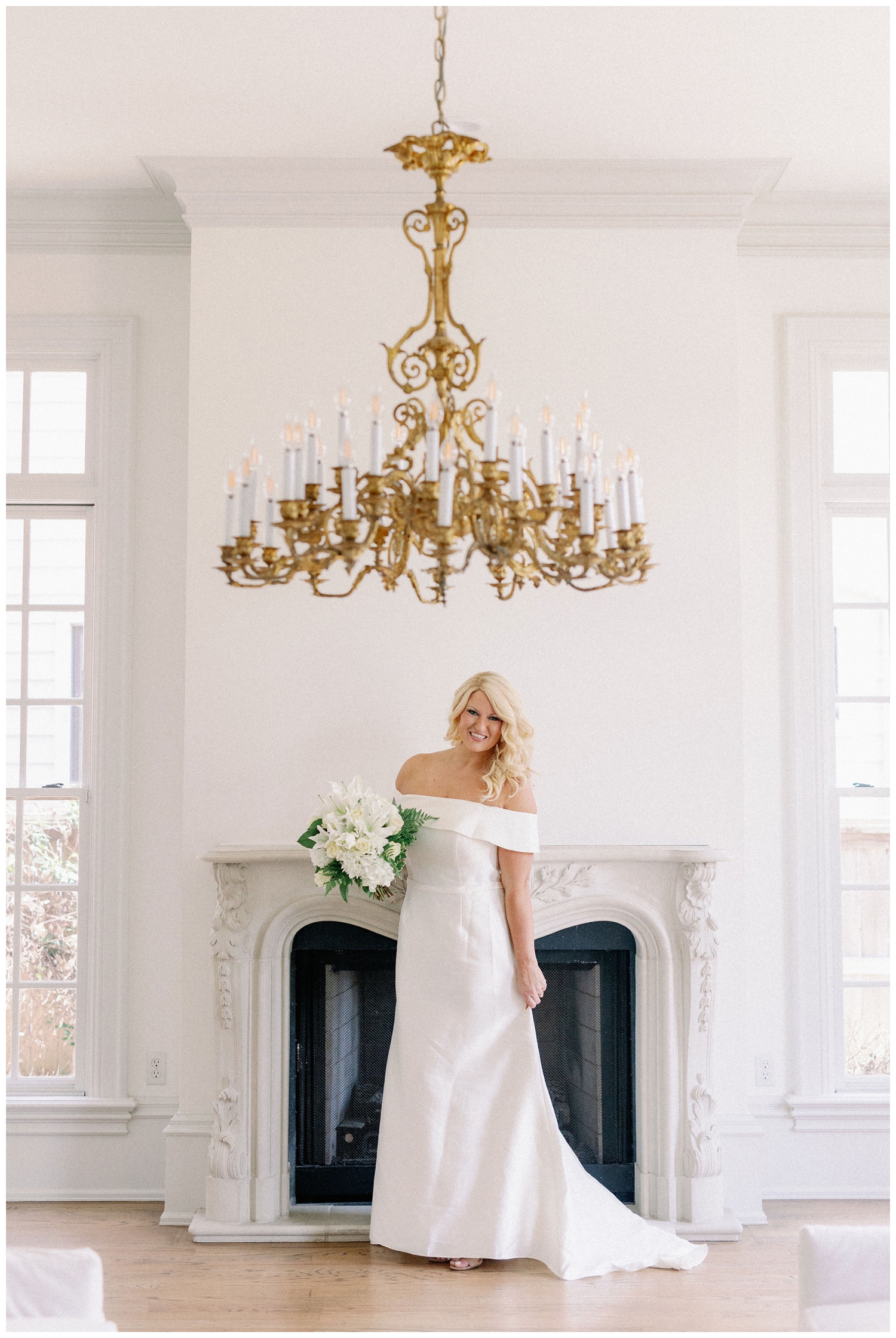 bride holding white bouquet posing in front of fireplace and chandelier at The Creative Chateau