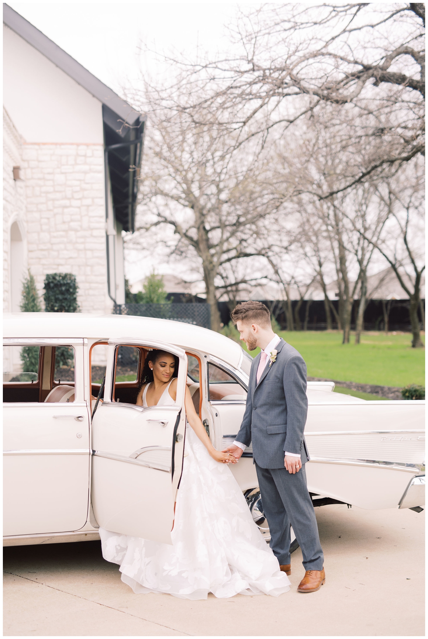 groom helping bride get out of white classic car in front of Brighton Abbey