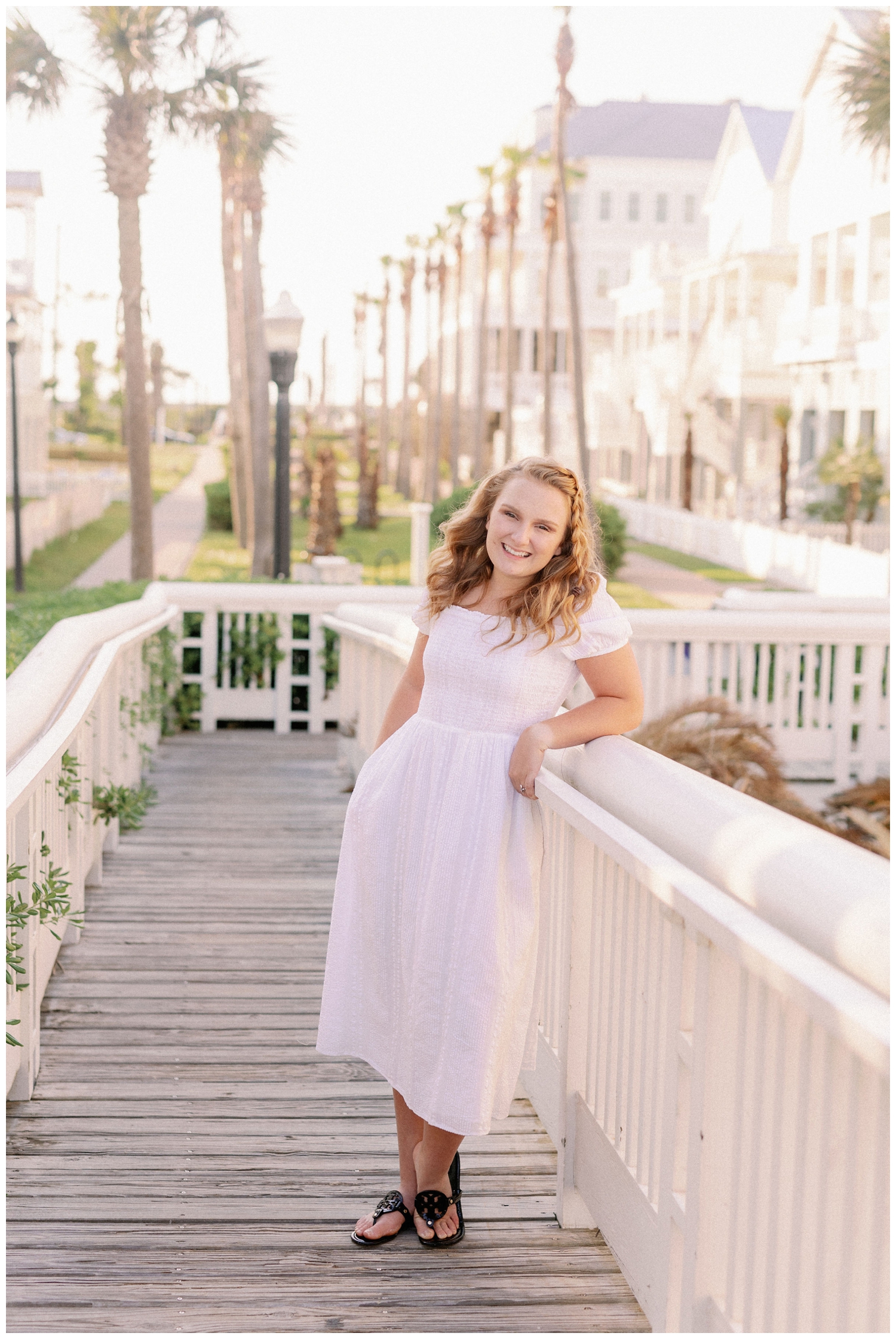 girl in white dress posing on boardwalk Galveston beach senior pictures