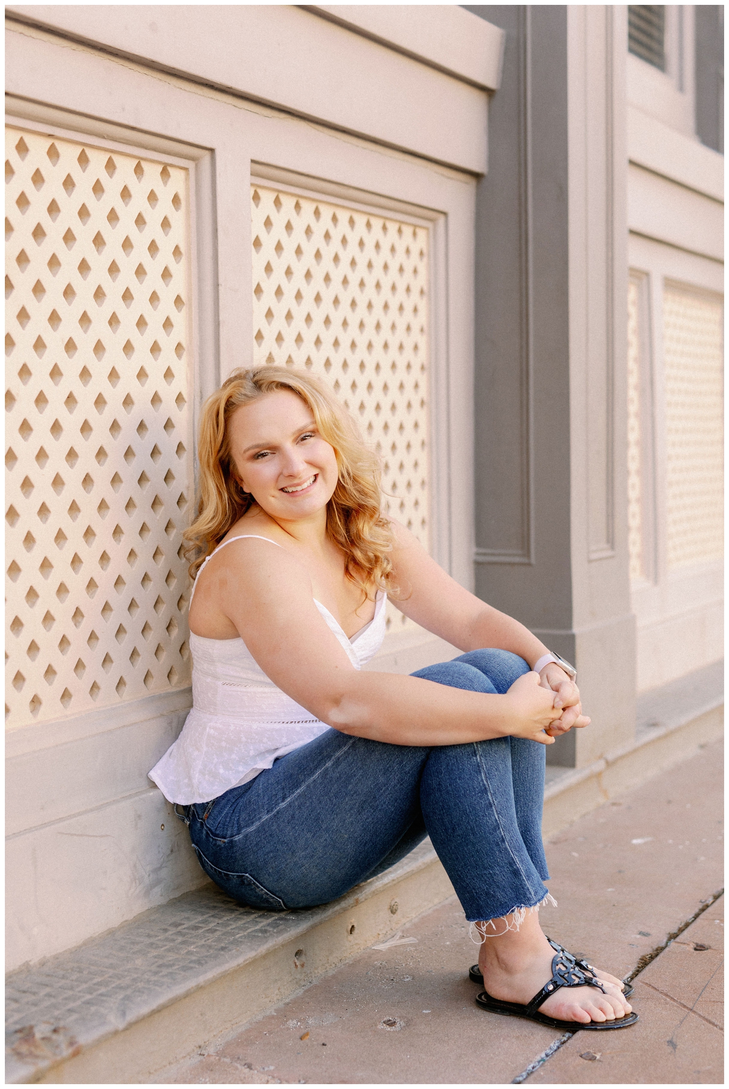 girl in jeans and white shirt sitting against a wall Galveston beach senior pictures