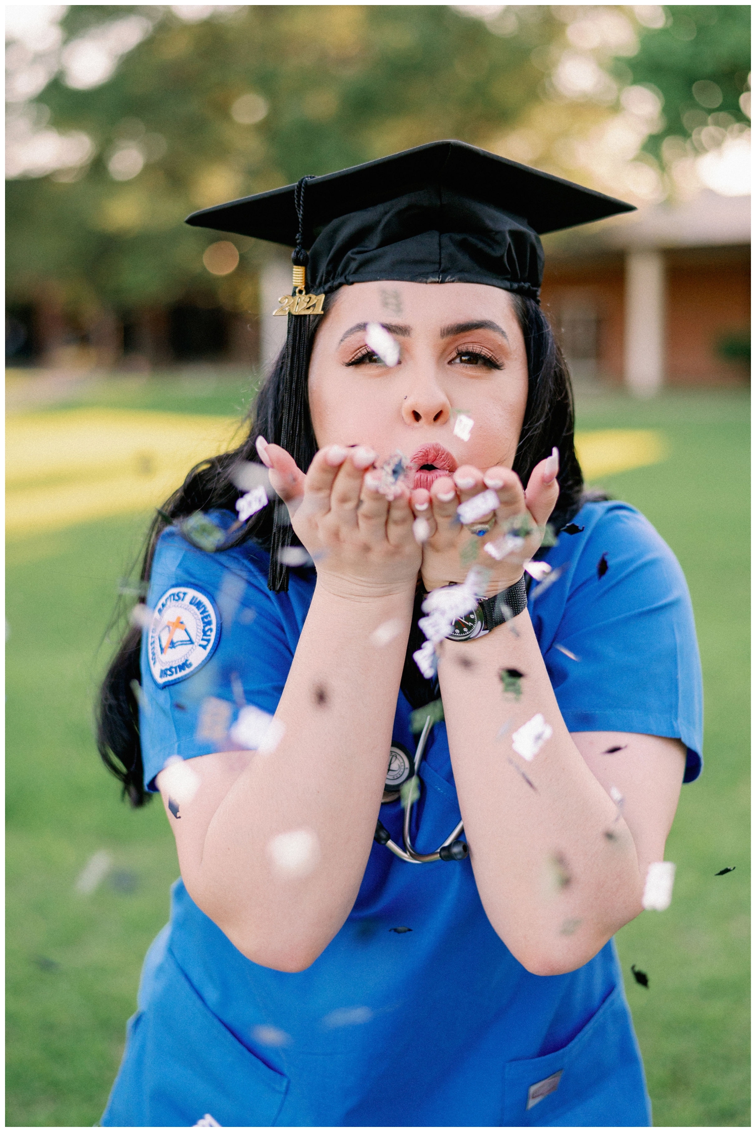 girl with graduation cap blowing confetti on lawn at Houston Baptist University senior photography