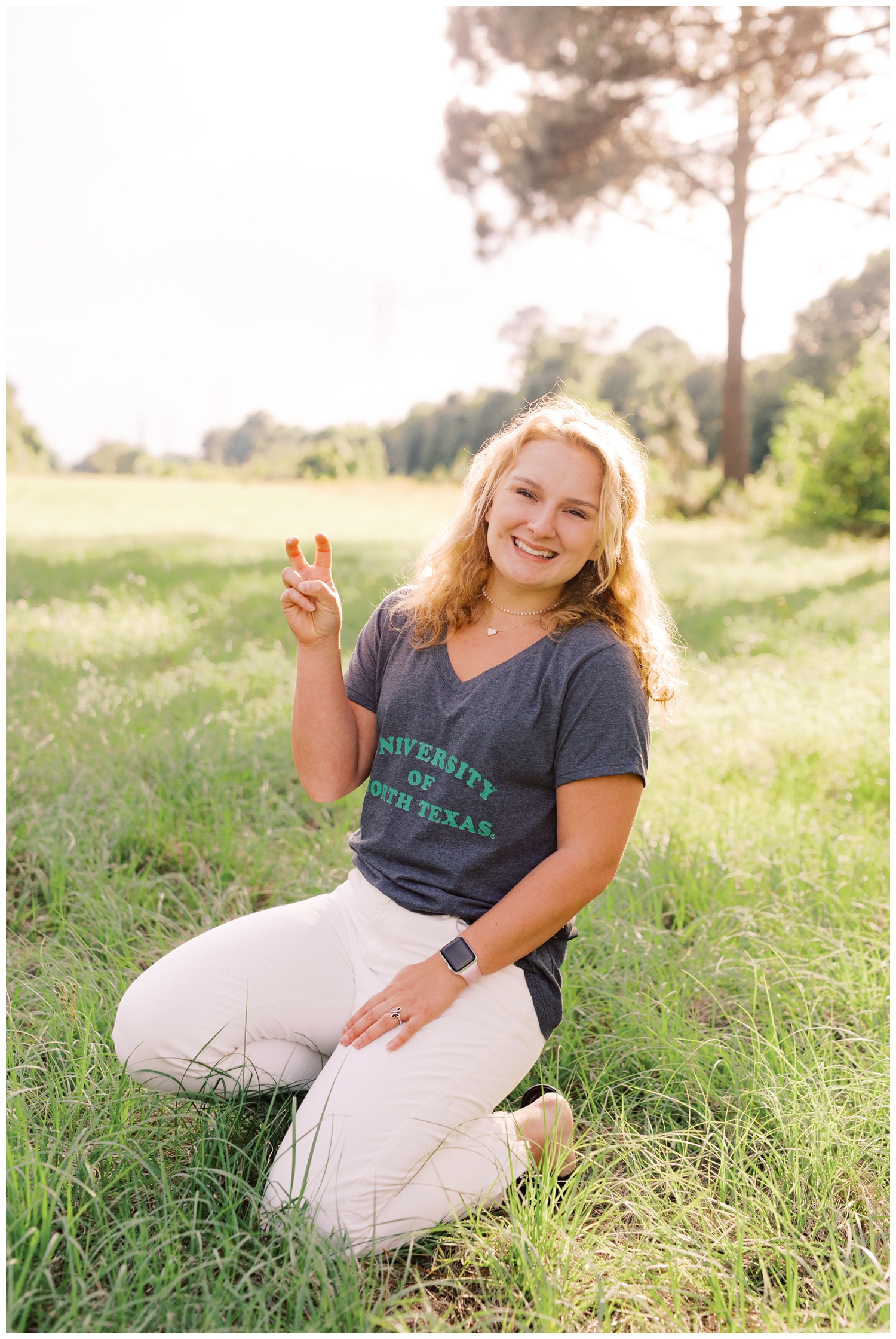 girl squatting in a field in her college tshirt for Houston Senior Model Team