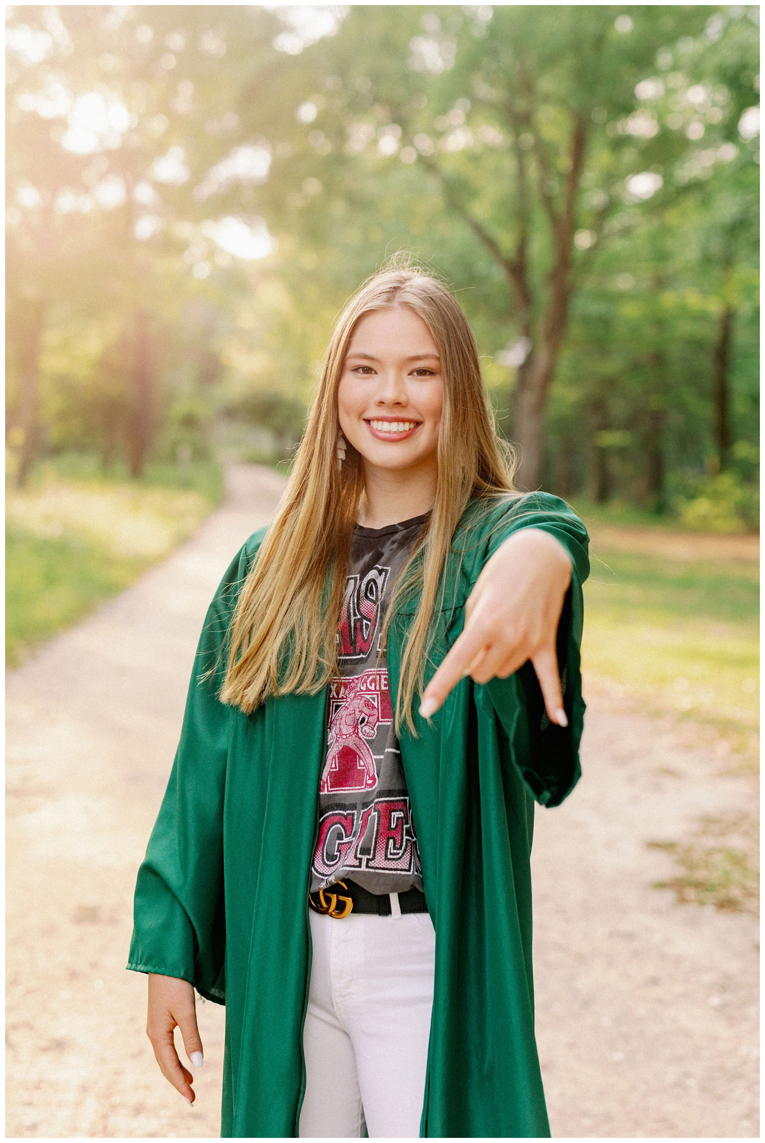 girl standing on sidewalk in graduation gown with horns down hand sign