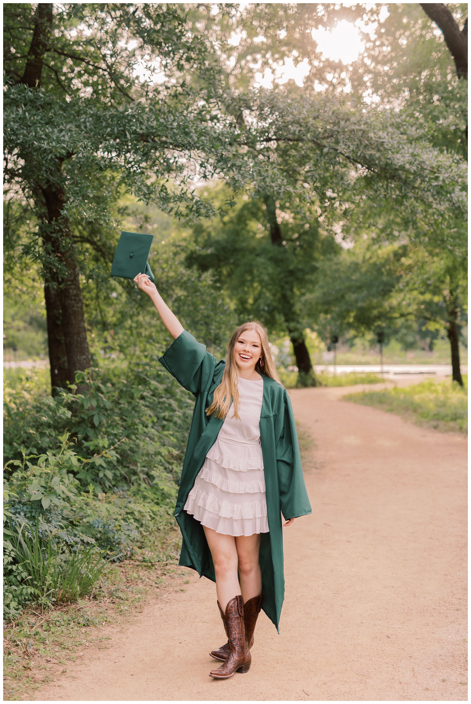 girl standing on sidewalk holding graduation cap in the air