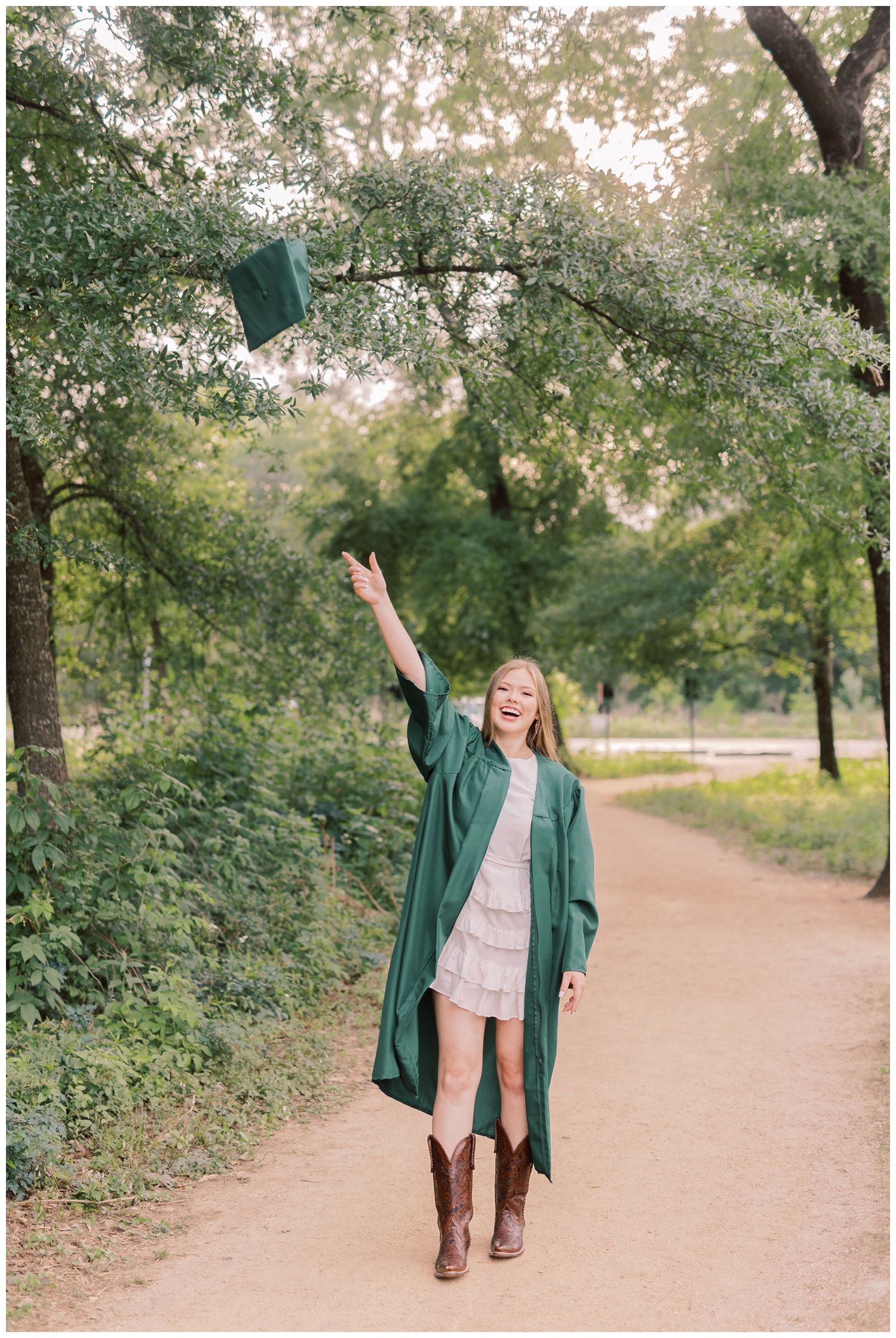 girl in emerald green graduation gown tossing her cap into the air