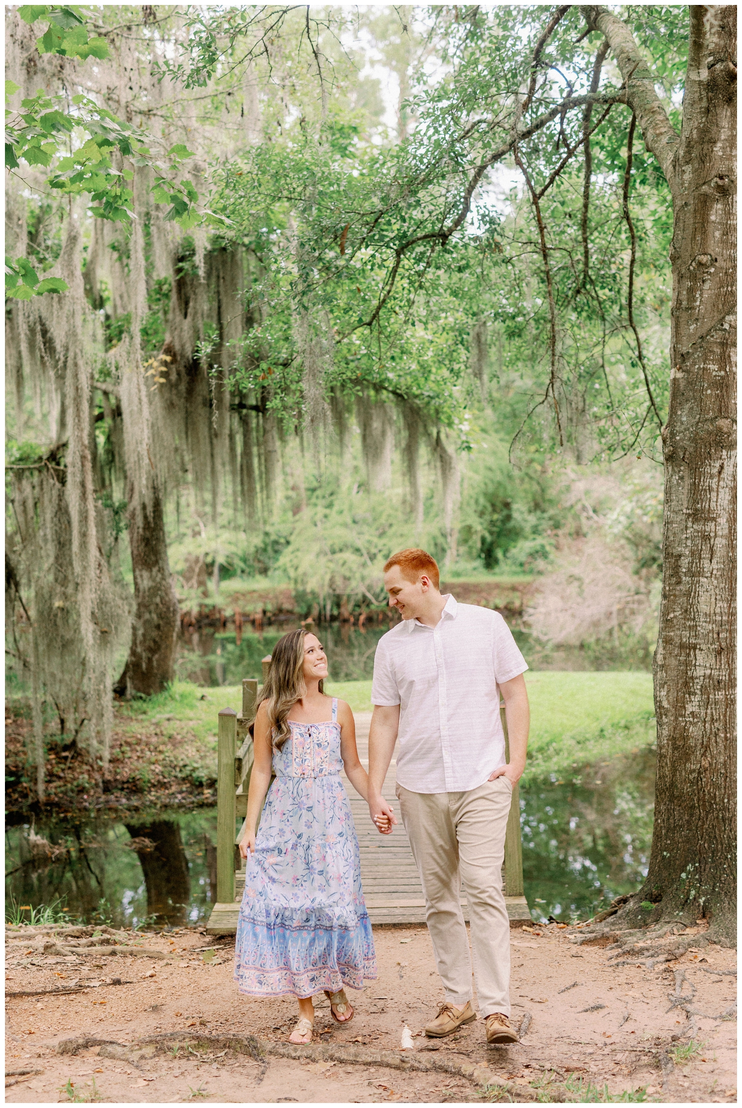 couple walking on bridge under mossy trees in Cypress Texas for Cypress engagement photographer