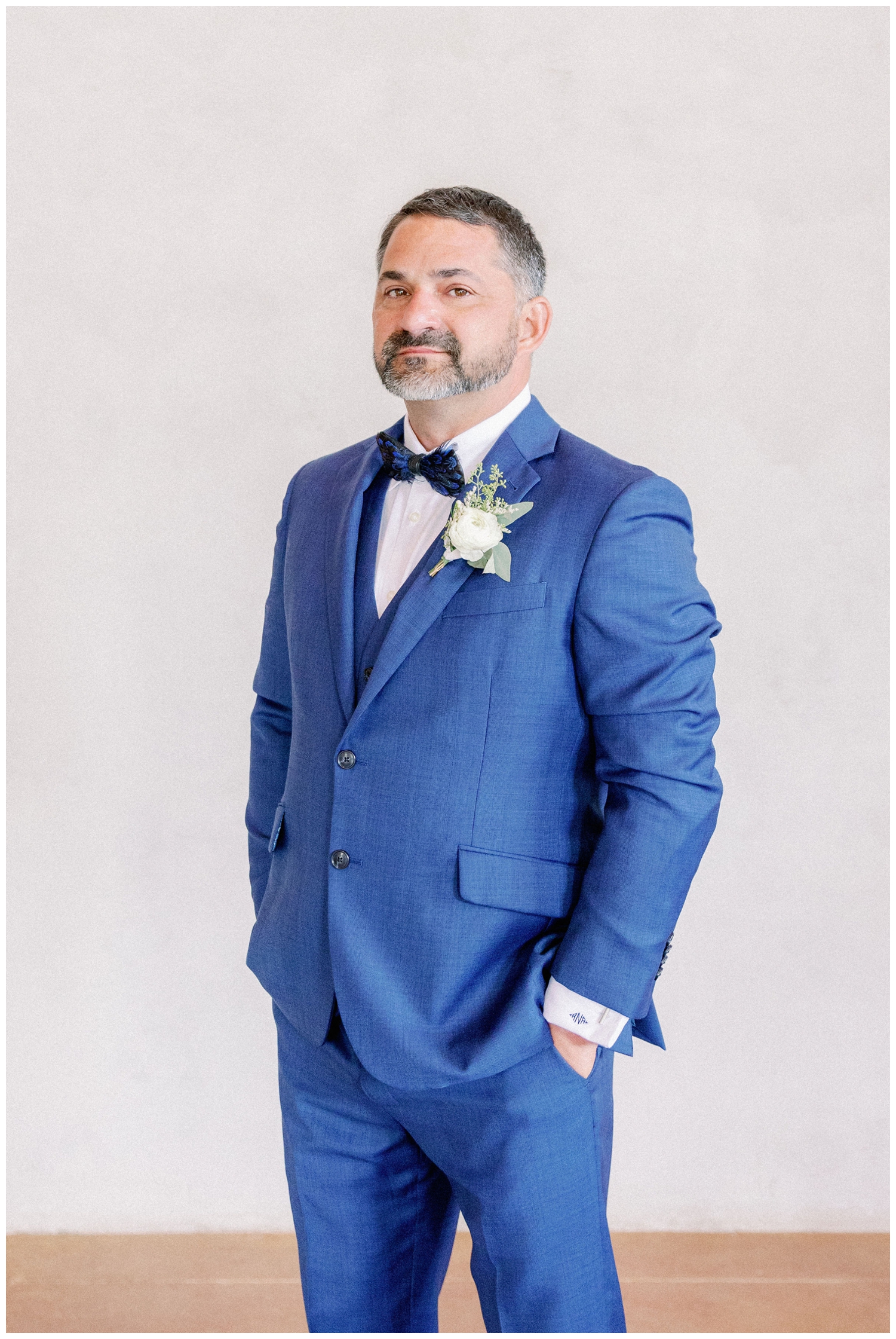 groom standing in blue tux with blue feather bow tie