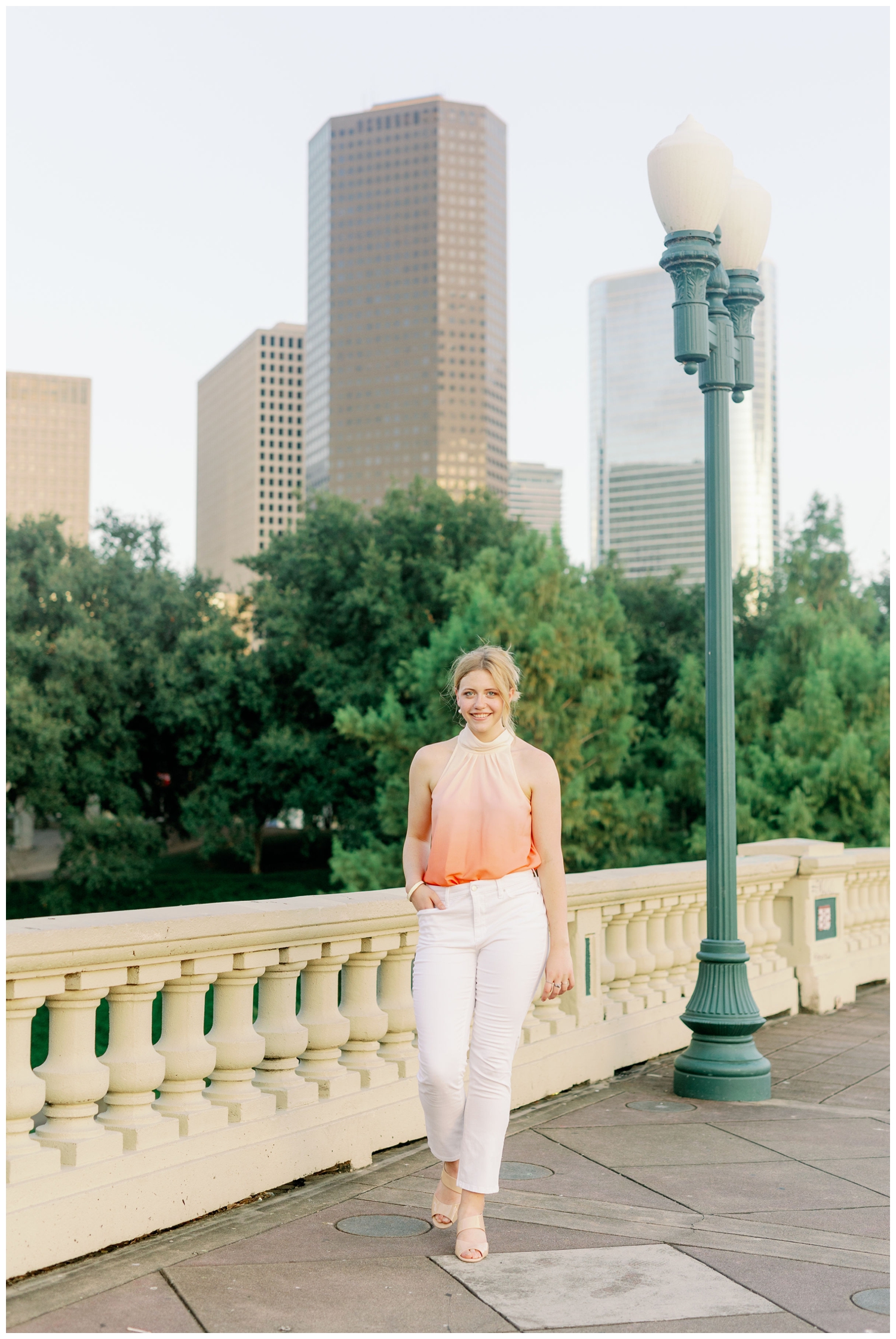senior girl in white pants walking on Sabine Bridge with downtown Houston skyline