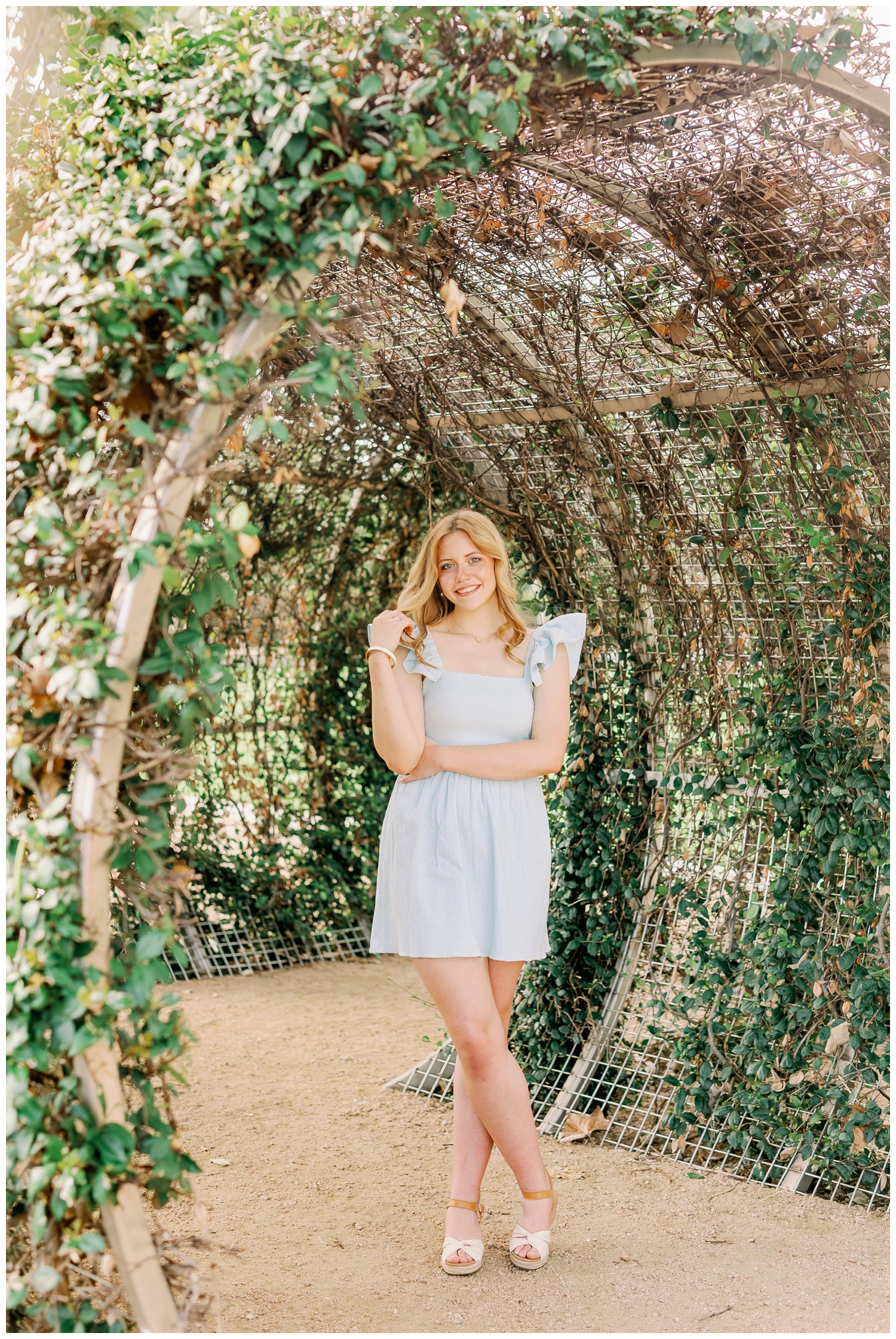 girl in blue dress standing in greenery arch at Sabine Street in downtown houston senior session