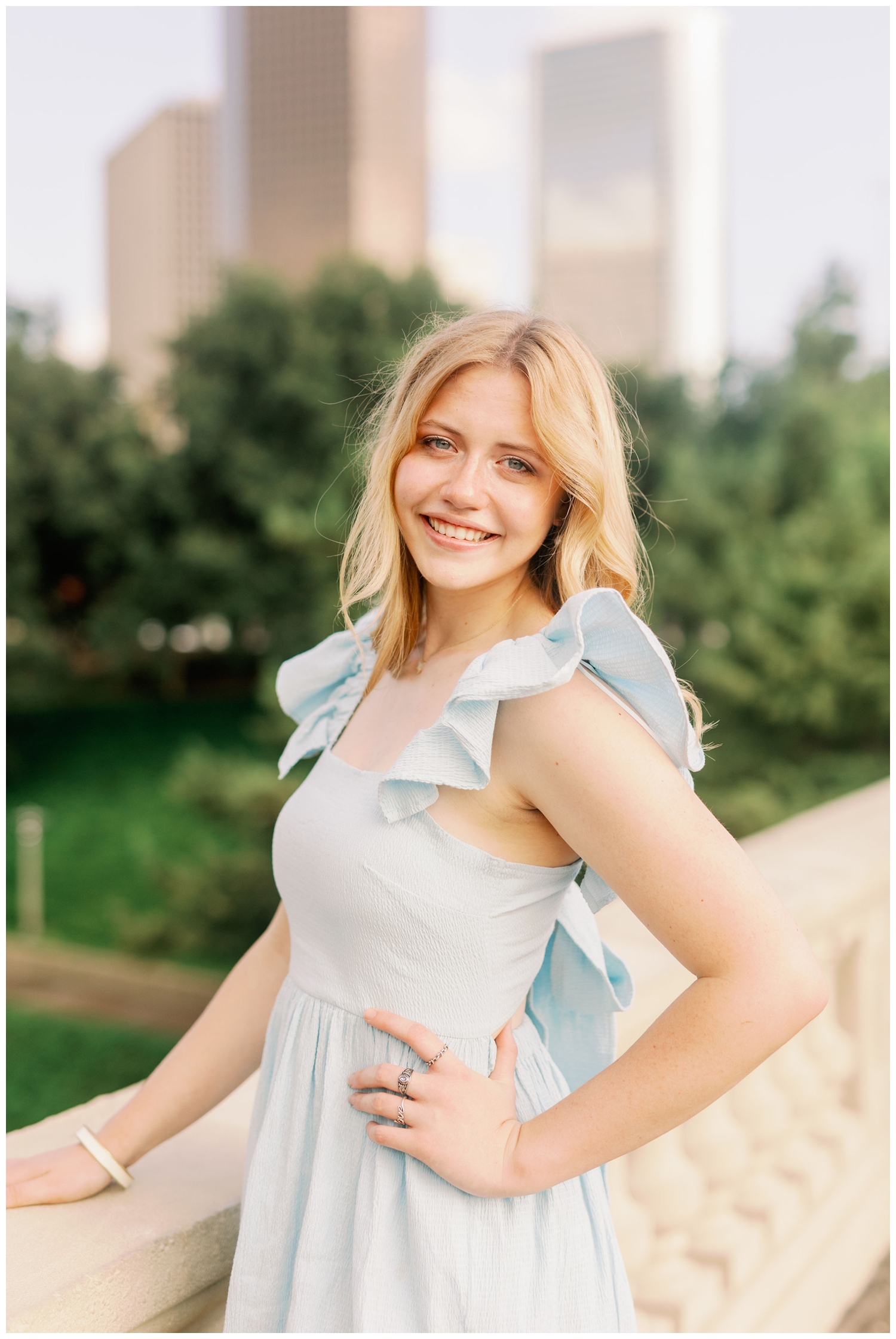 girl standing in front of downtown Houston Skyline in blue dress with hand on bridge