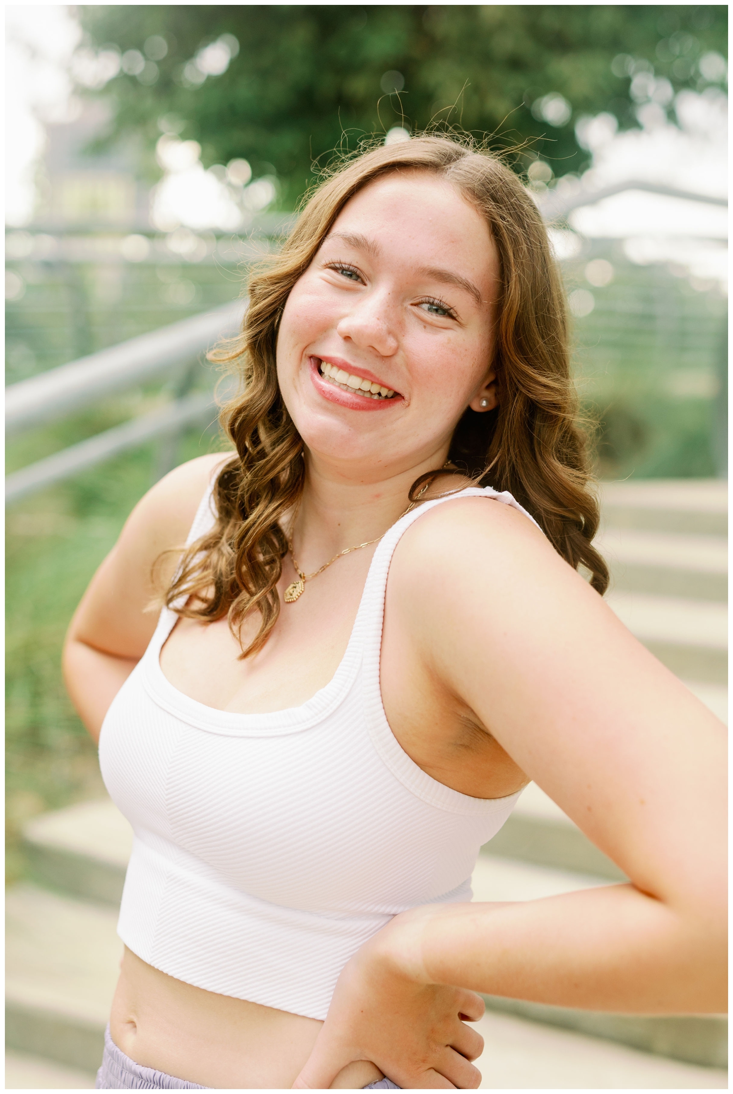 girl in white tank smiling at camera with hands on hip
