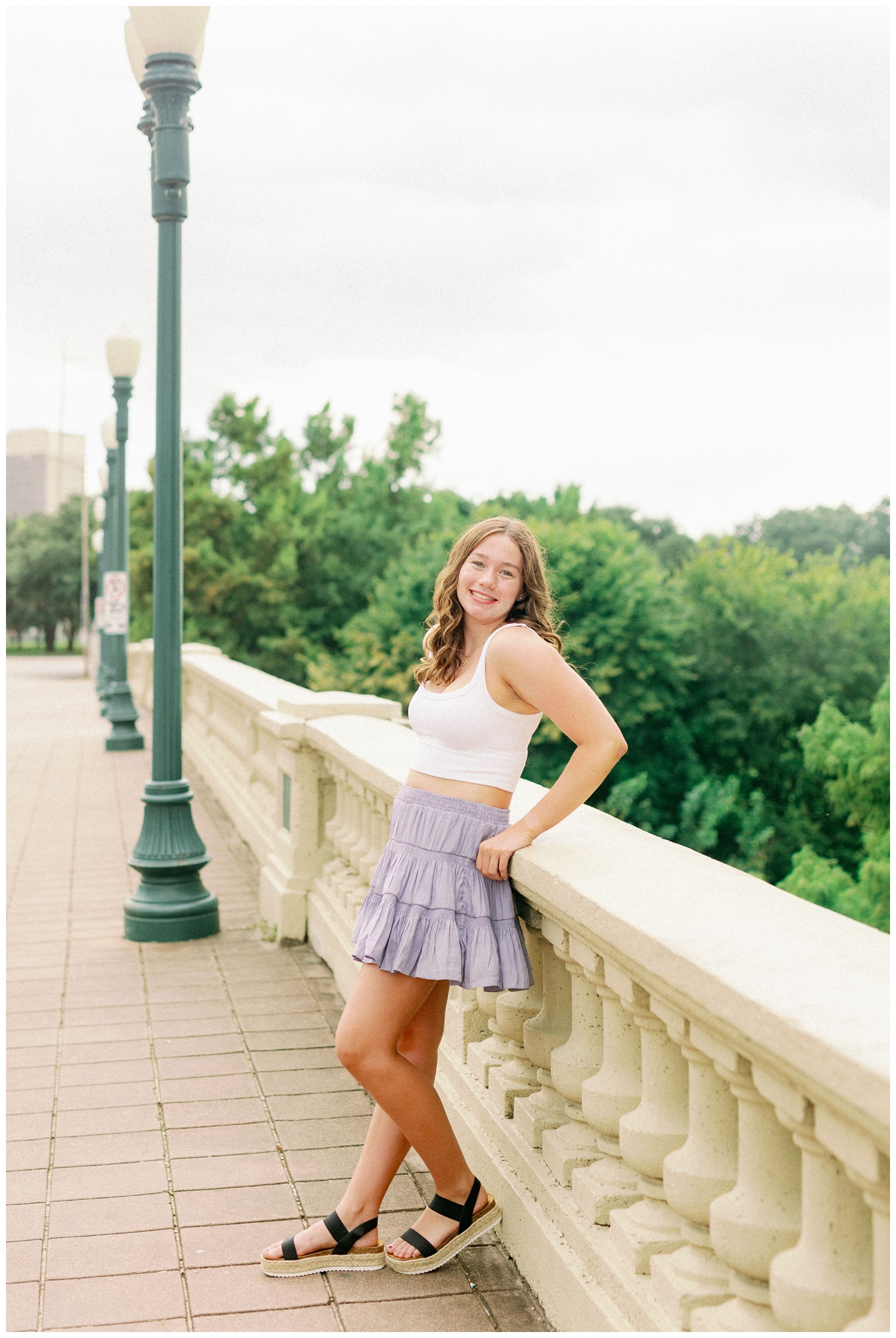 girl leaning on Sabine bridge in blue skirt and white tank shirt Houston senior photos