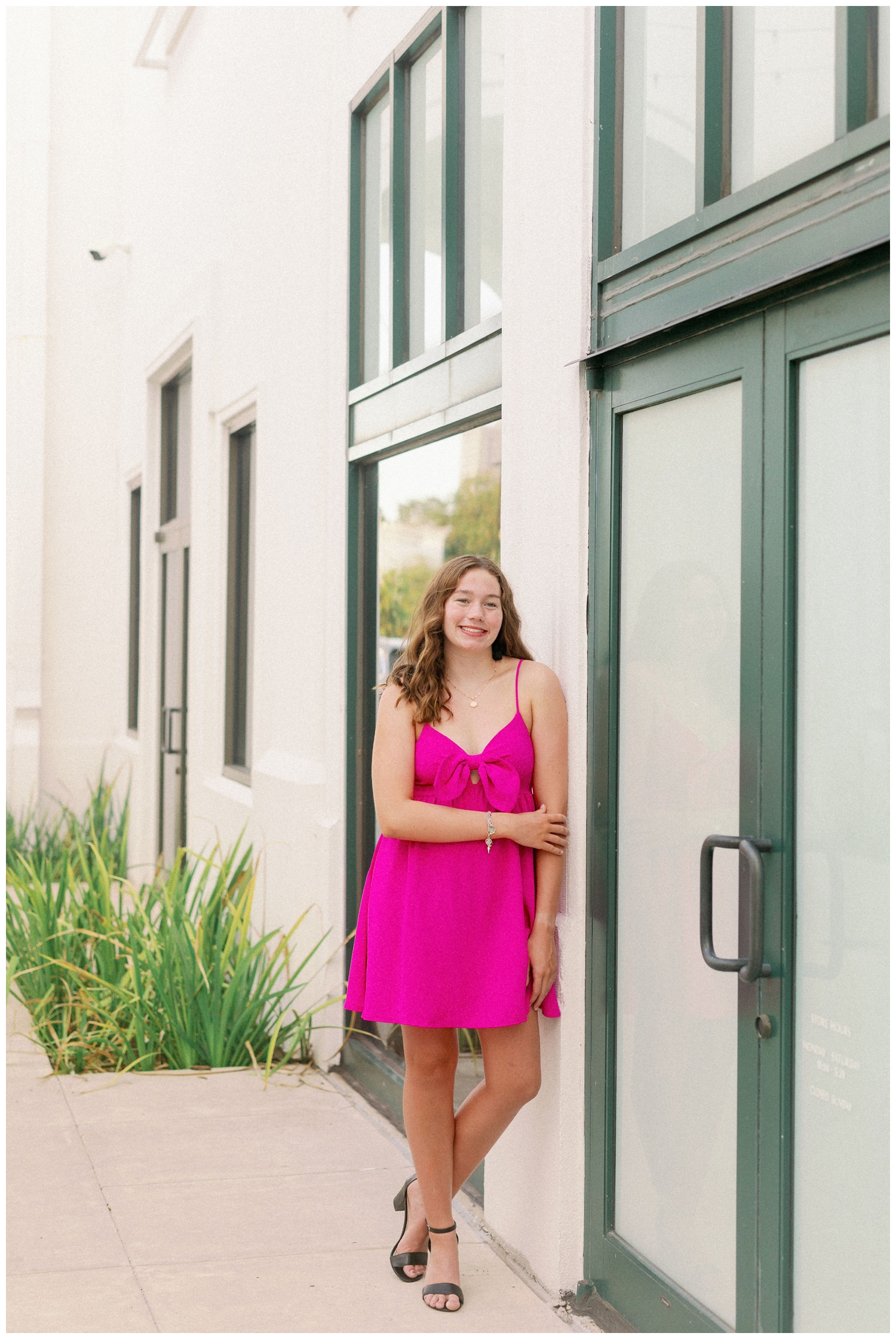 Houston senior in hot pink dress leaning against a wall at Uptown Park