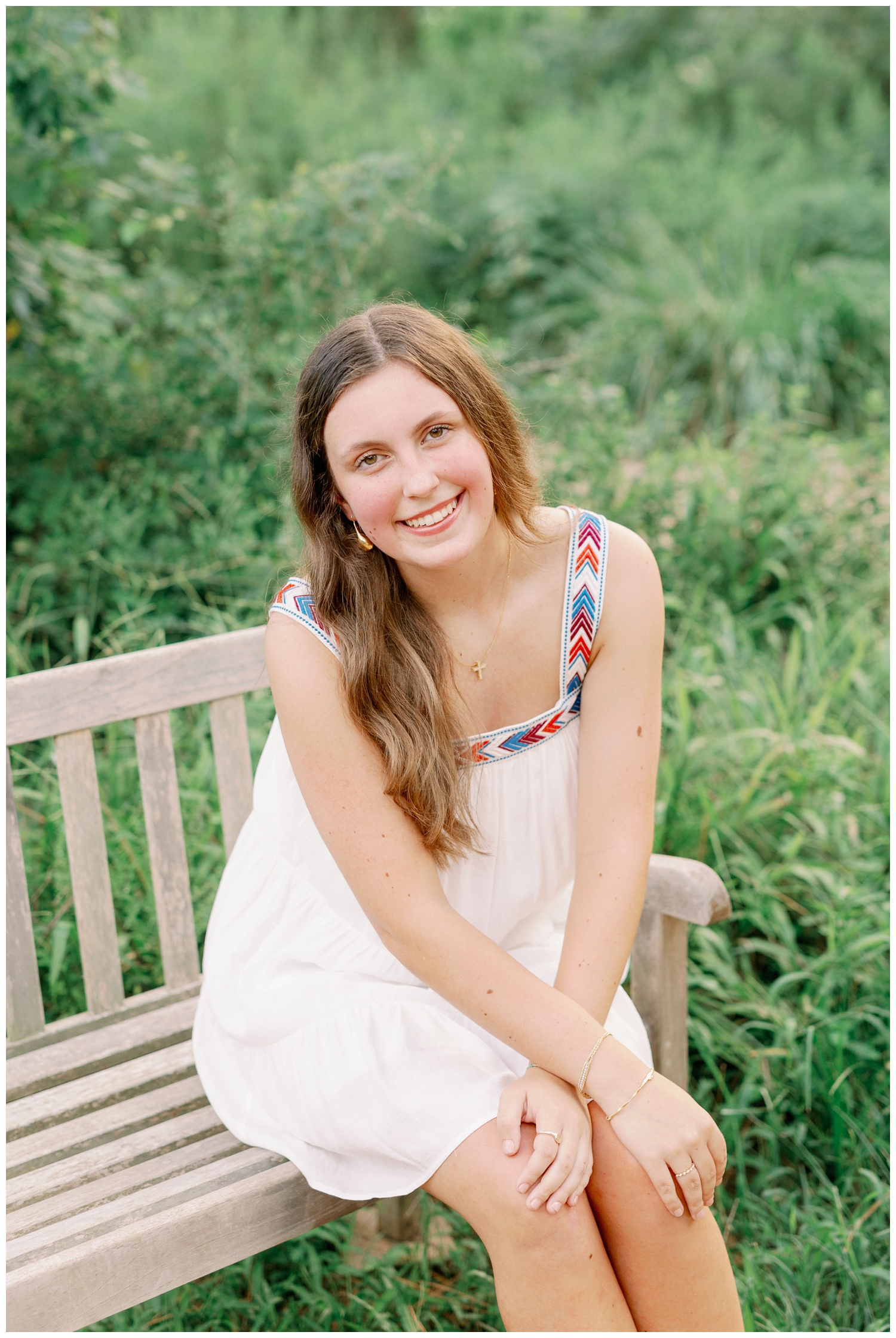 senior girl in white dress sitting on bench in front of field
