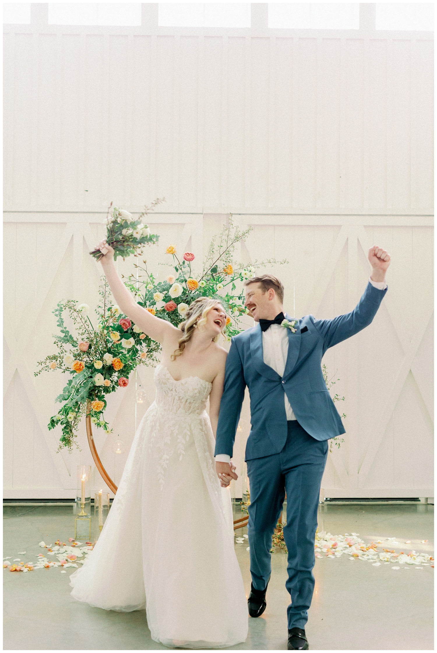 bride and groom cheering standing in front of floral hoop installation inside reception space at The Farmhouse Wedding and Event Venue