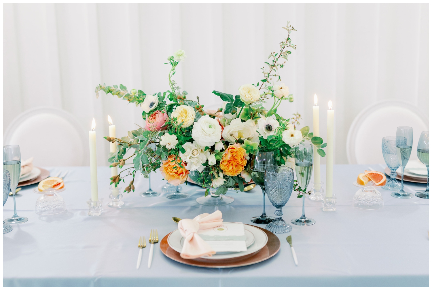 reception table with baby blue linen and blush place setting and bright florals inside The Farmhouse Wedding and Event Venue in Montgomery, Texas