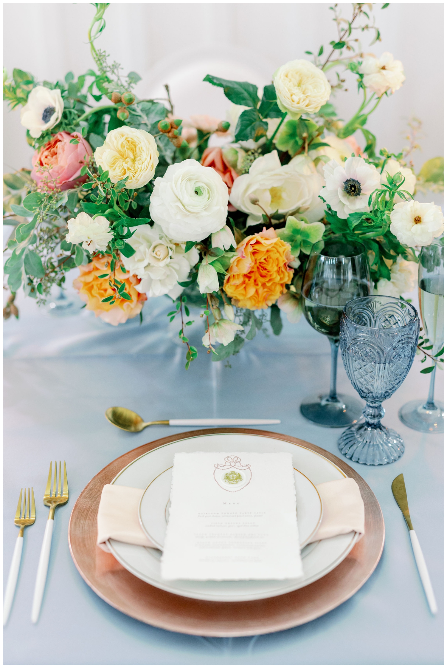 blush place setting with white menu card on blue table cloth with light blue stemware and peonies