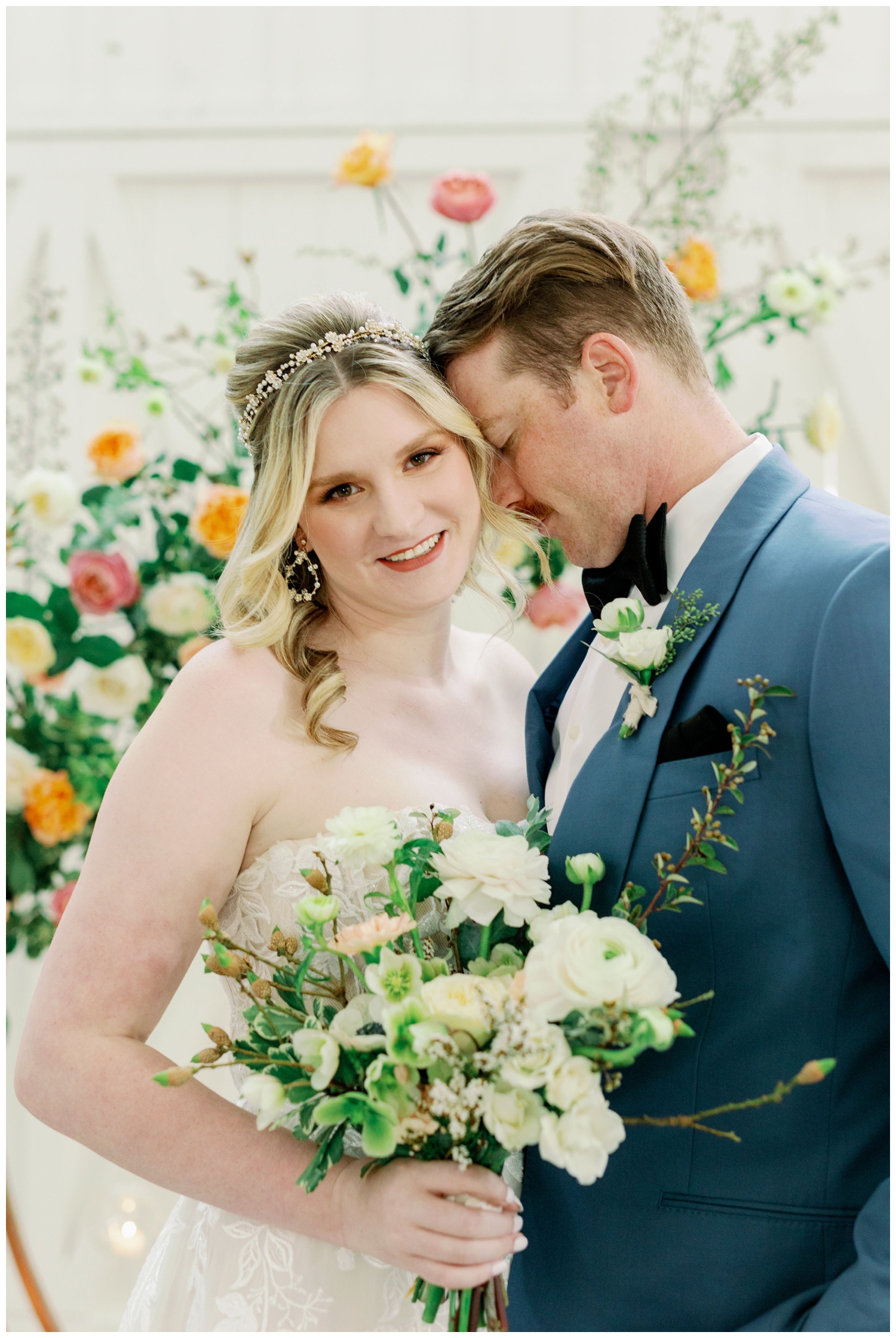 bride and groom nuzzling in front of bright florals on a gold hoop The Farmhouse Wedding and Event Venue