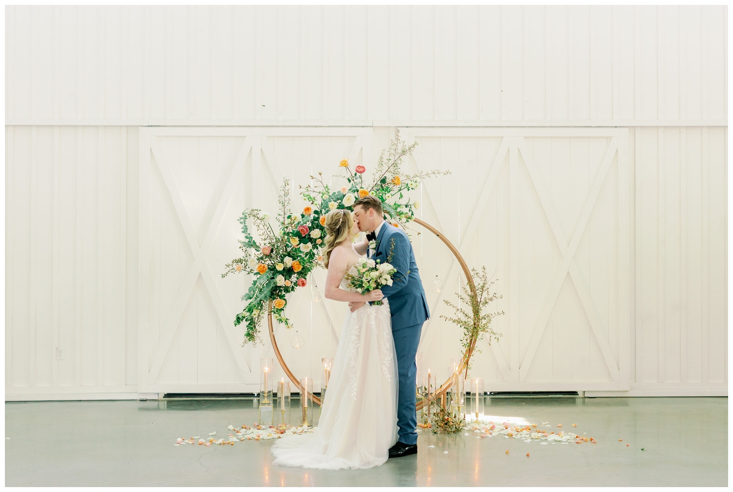 bride and groom kissing The Farmhouse Wedding and Event Venue in front of gold hoop with bright florals