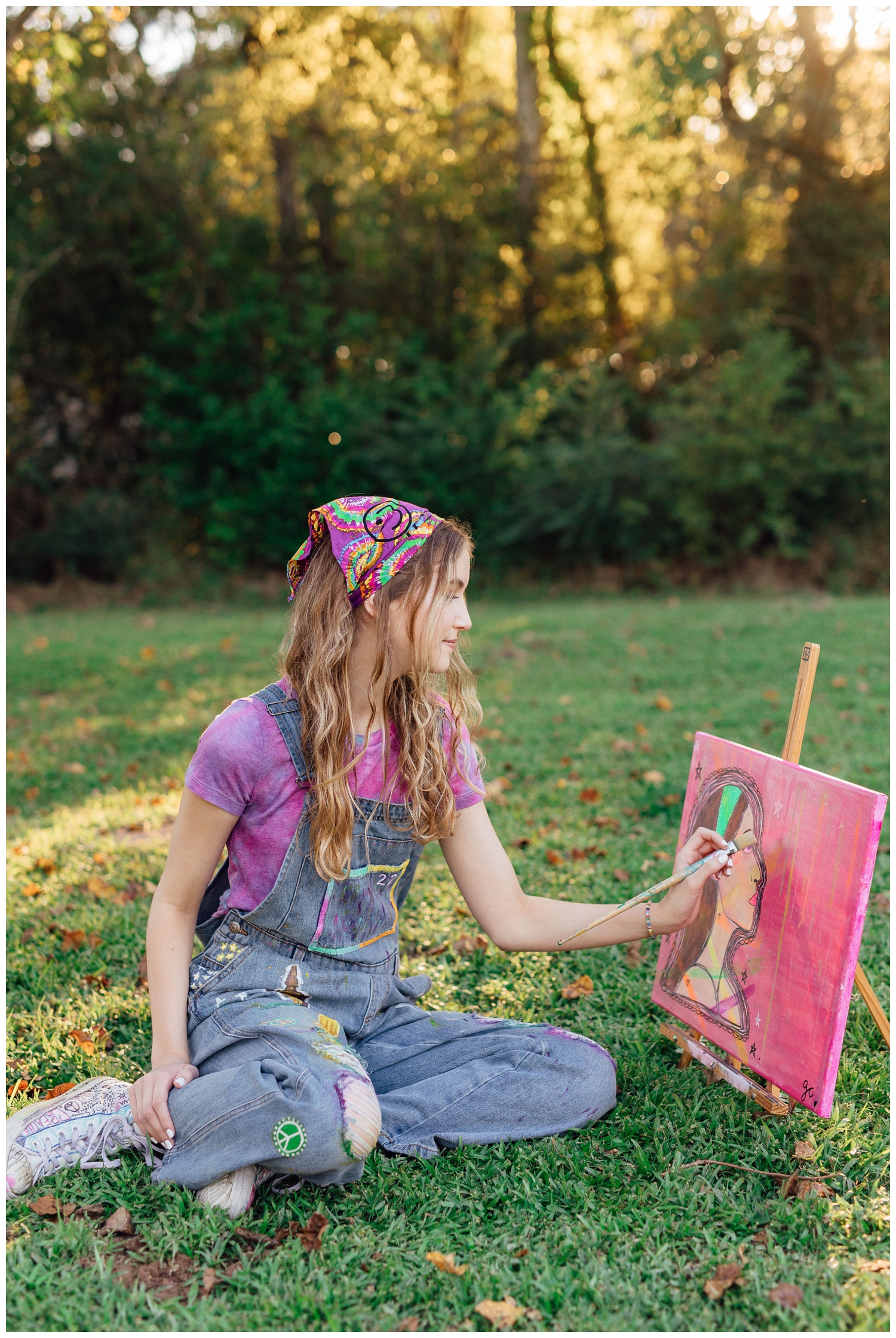 colorful Houston senior photos with girl in denim overalls sitting under a tree painting