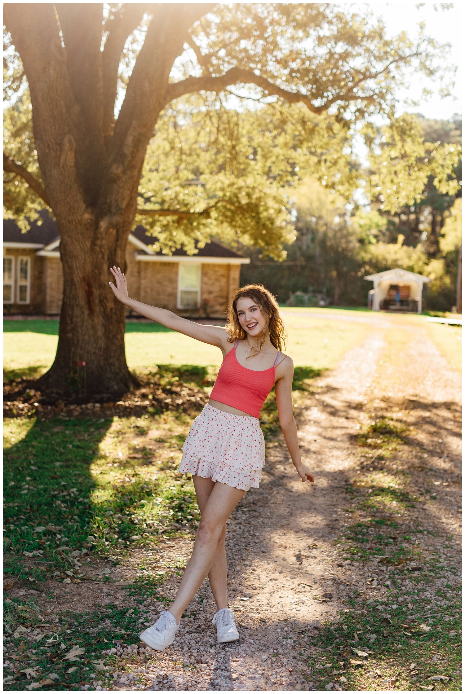 girl in coral top and white skirt kicking leg standing under a tree in Cypress Texas