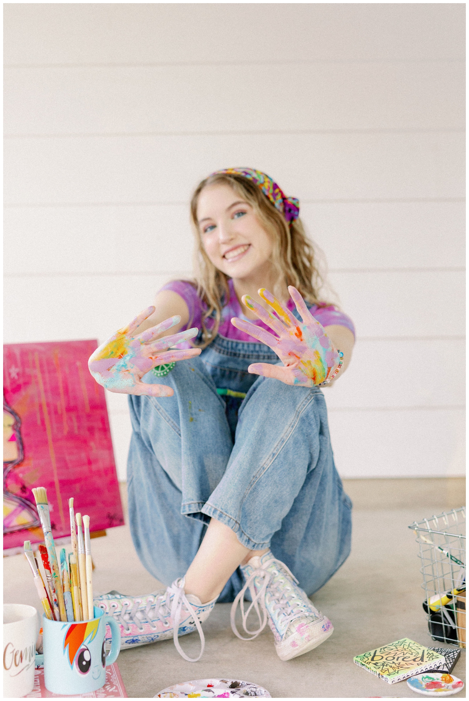 senior girl in denim overalls holding painted hands out for colorful Houston senior photos