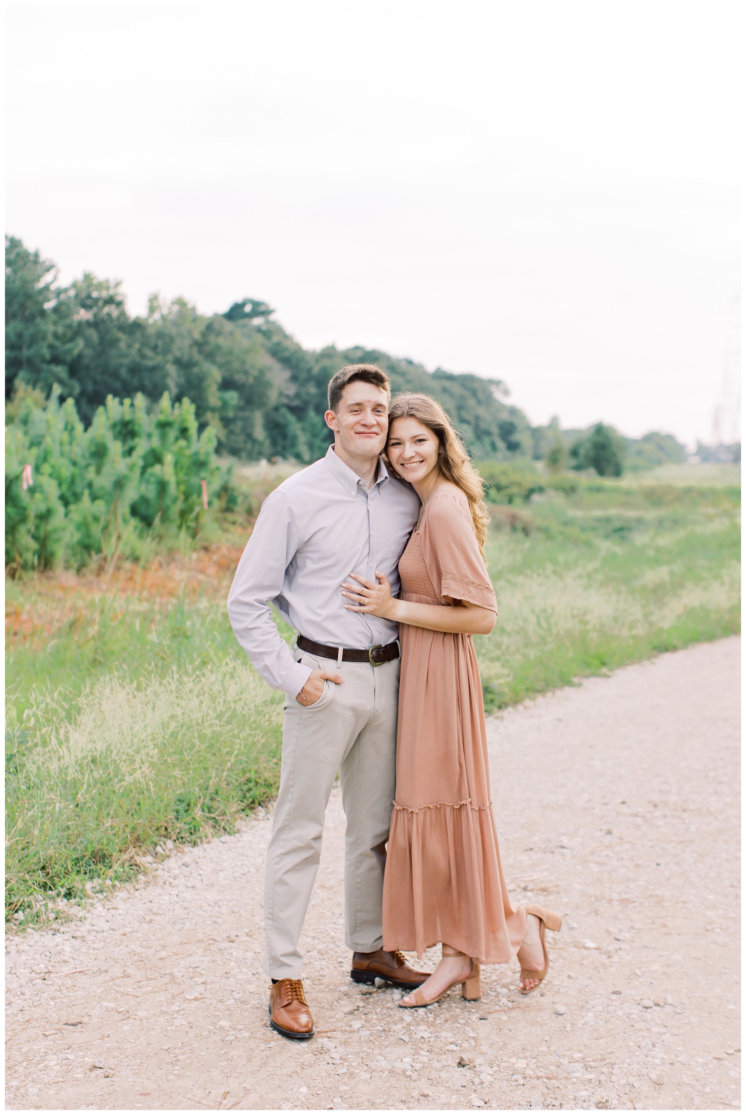 couple in coral dress and khaki pants standing on pathway at Cy-Hope Cypress engagement photos