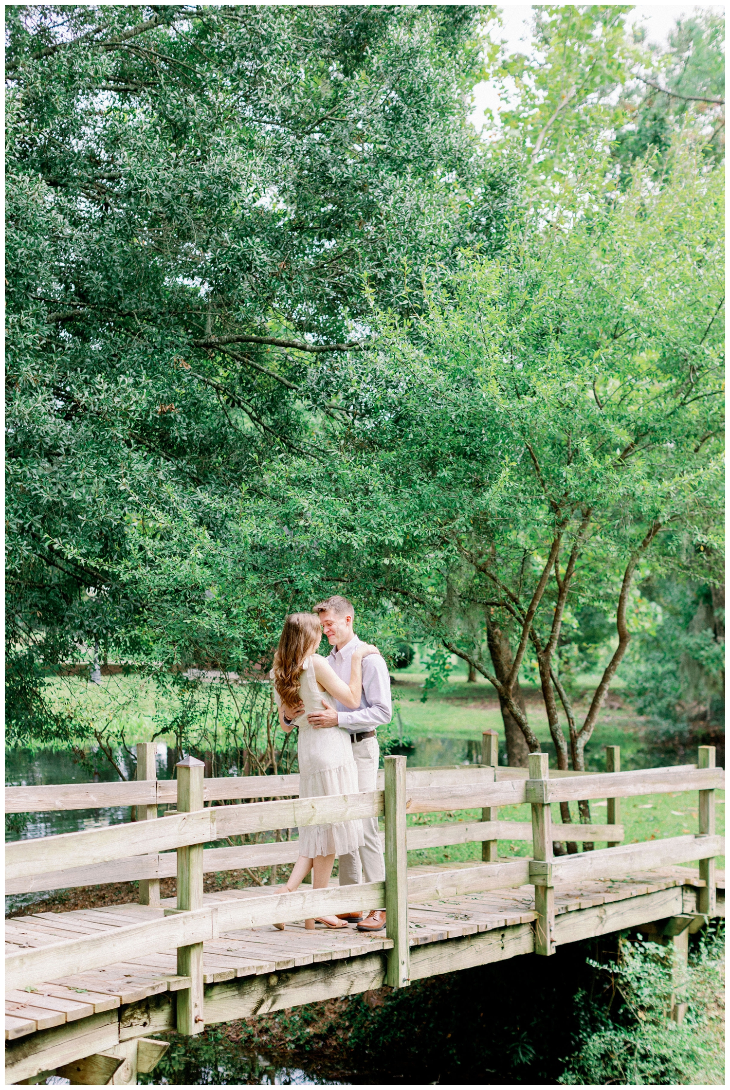 engaged couple standing on a bridge under green trees at Cy-Hope in Cypress Texas