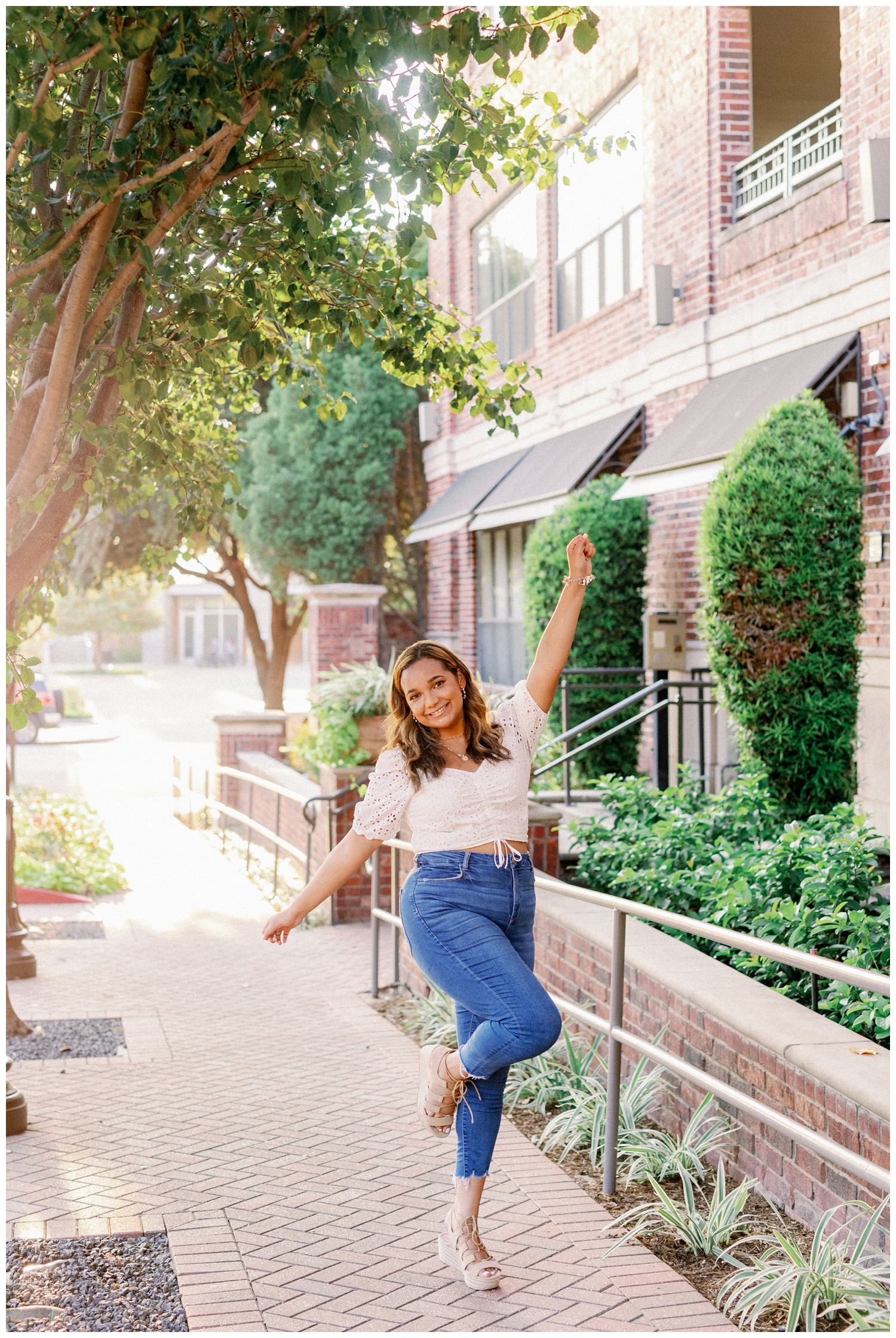 Houston senior photos of girl in blue jeans and white shirt on standing on sidewalk with hands in the air