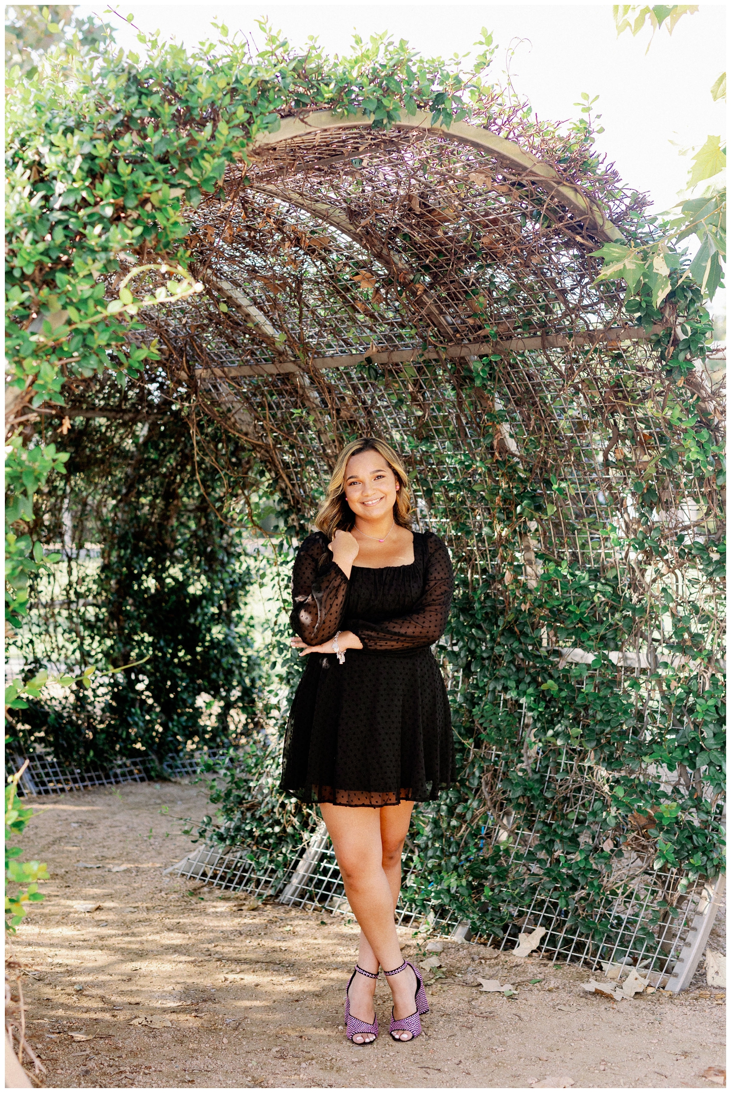 Houston senior photos with girl in black dress standing with arms crossed under ivy arch